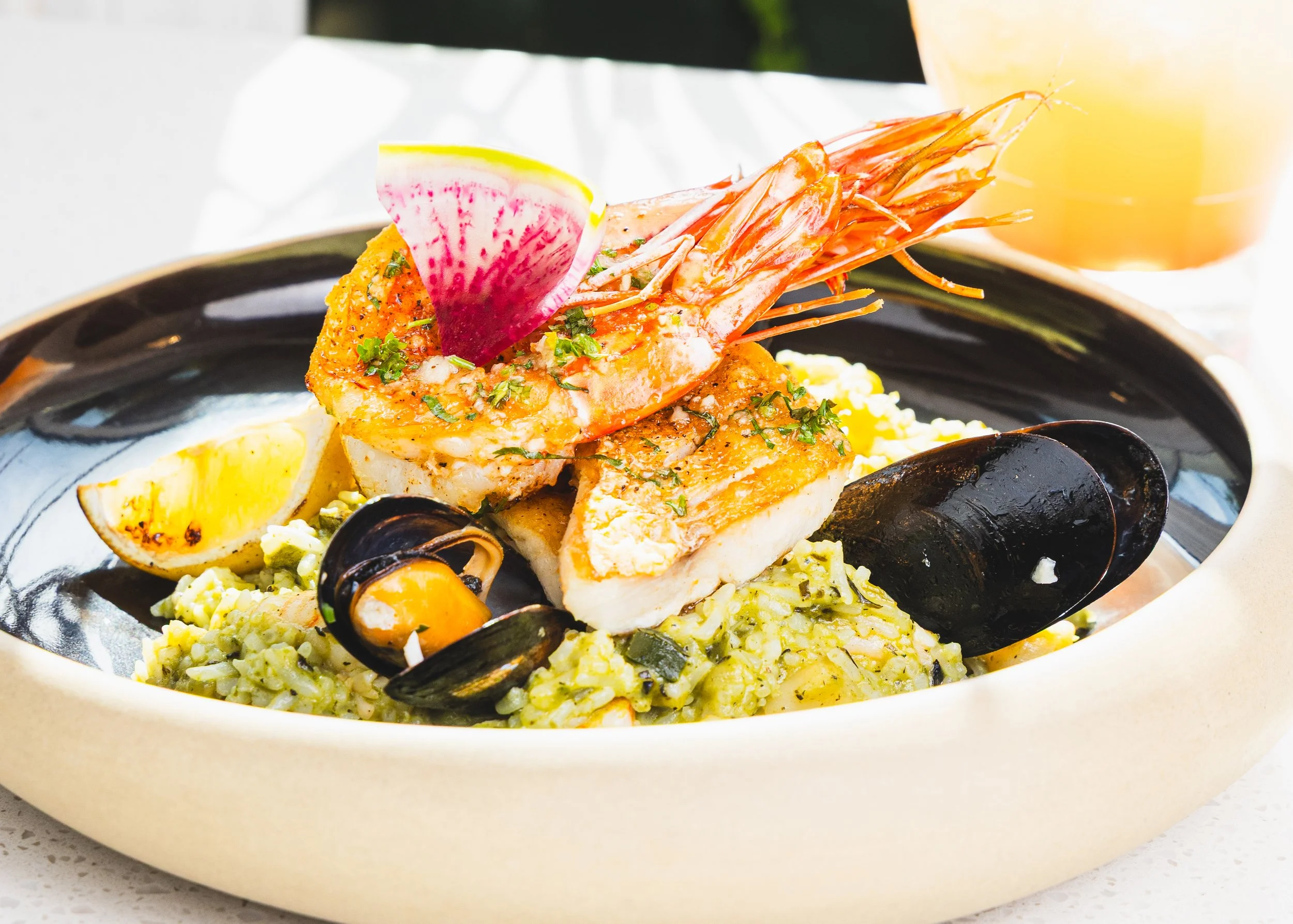 Seafood risotto with large grilled shrimp, mussels in shell, lemon wedge, and chopped herbs on top.