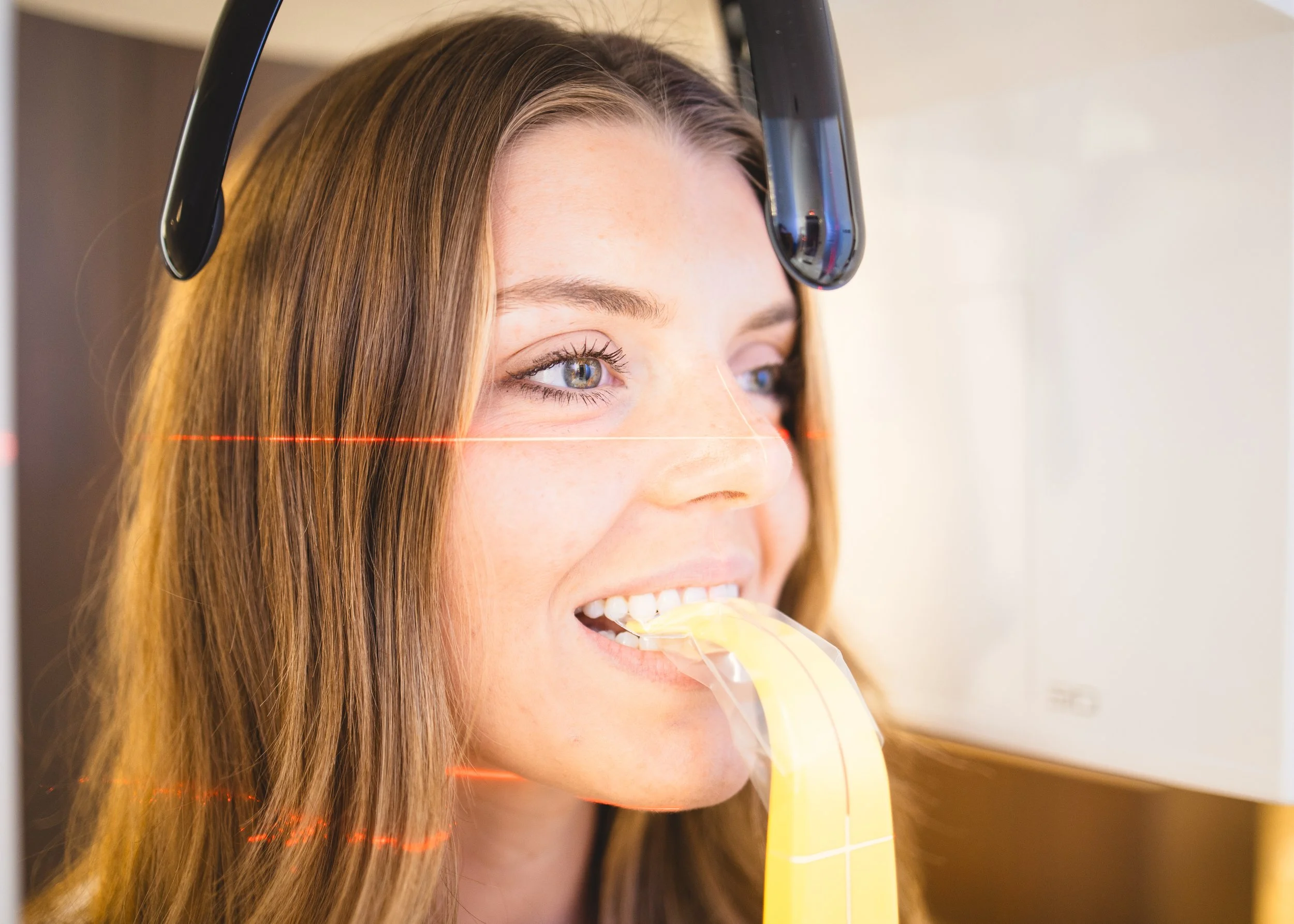 Close-up of a young woman's face during a laser eye scan, with laser lines projected onto her face, as a device hovers over her eye.
