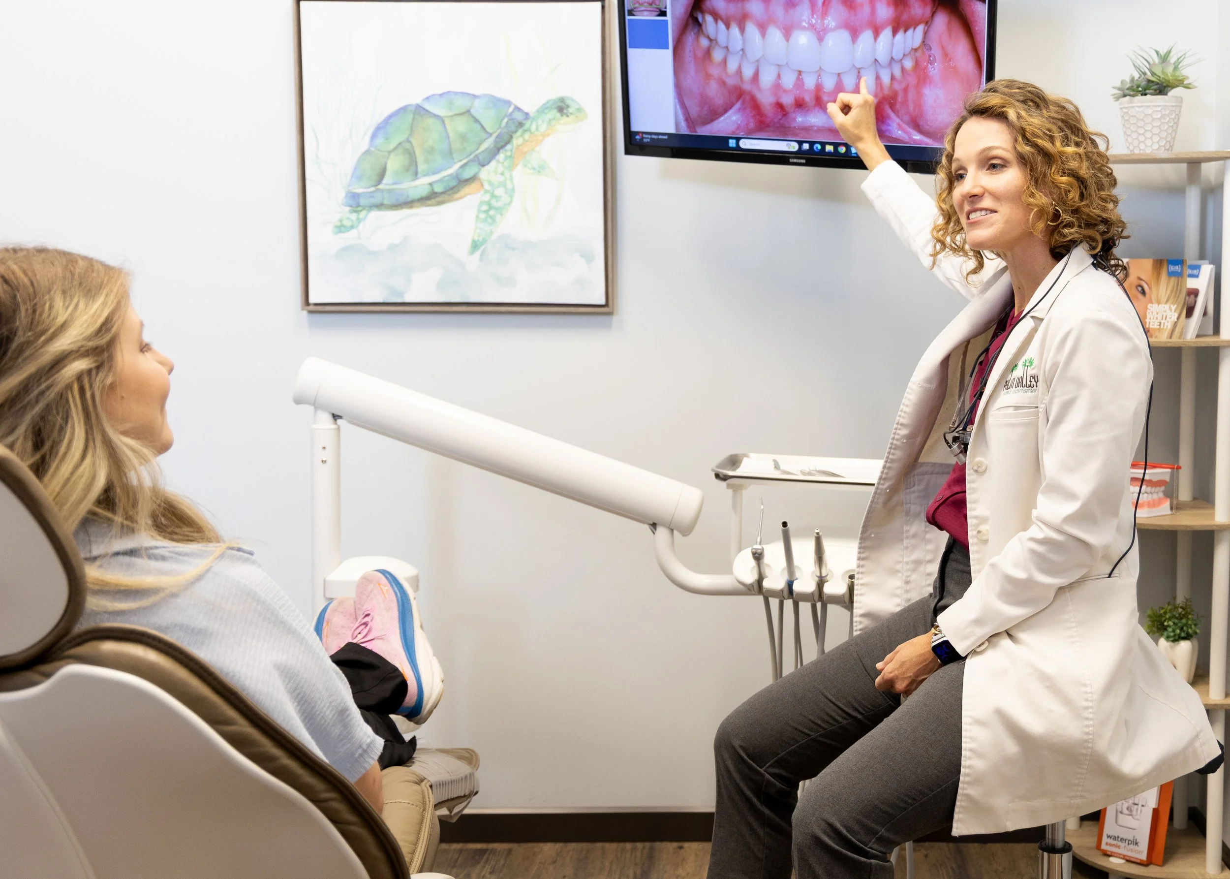 Dental professional discussing teeth images with a female patient in a dental office.