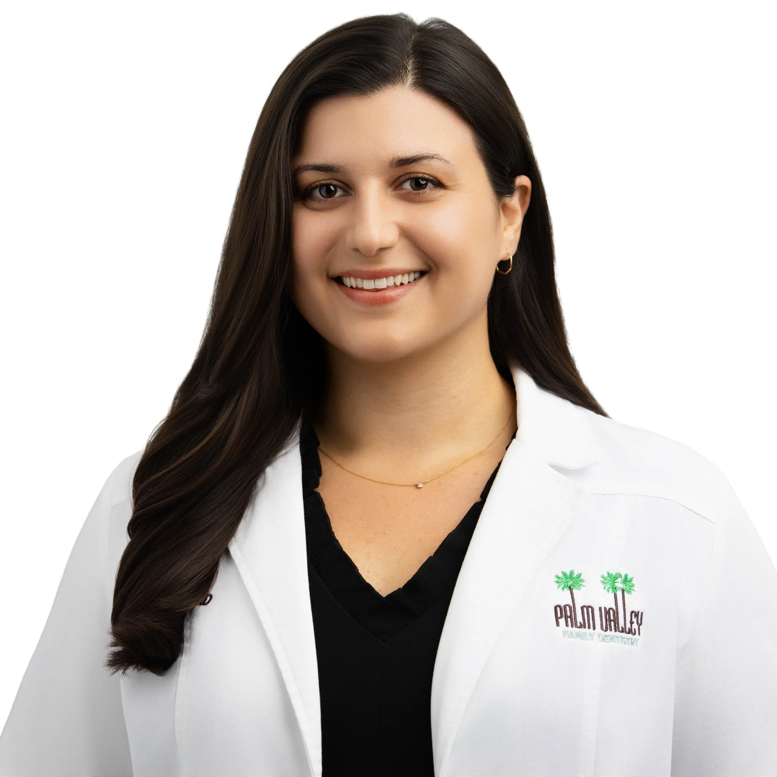 A smiling woman with long dark hair, wearing a white lab coat with palm trees and 'Palm Valley Family Dentistry' embroidered on it, standing against a white background.