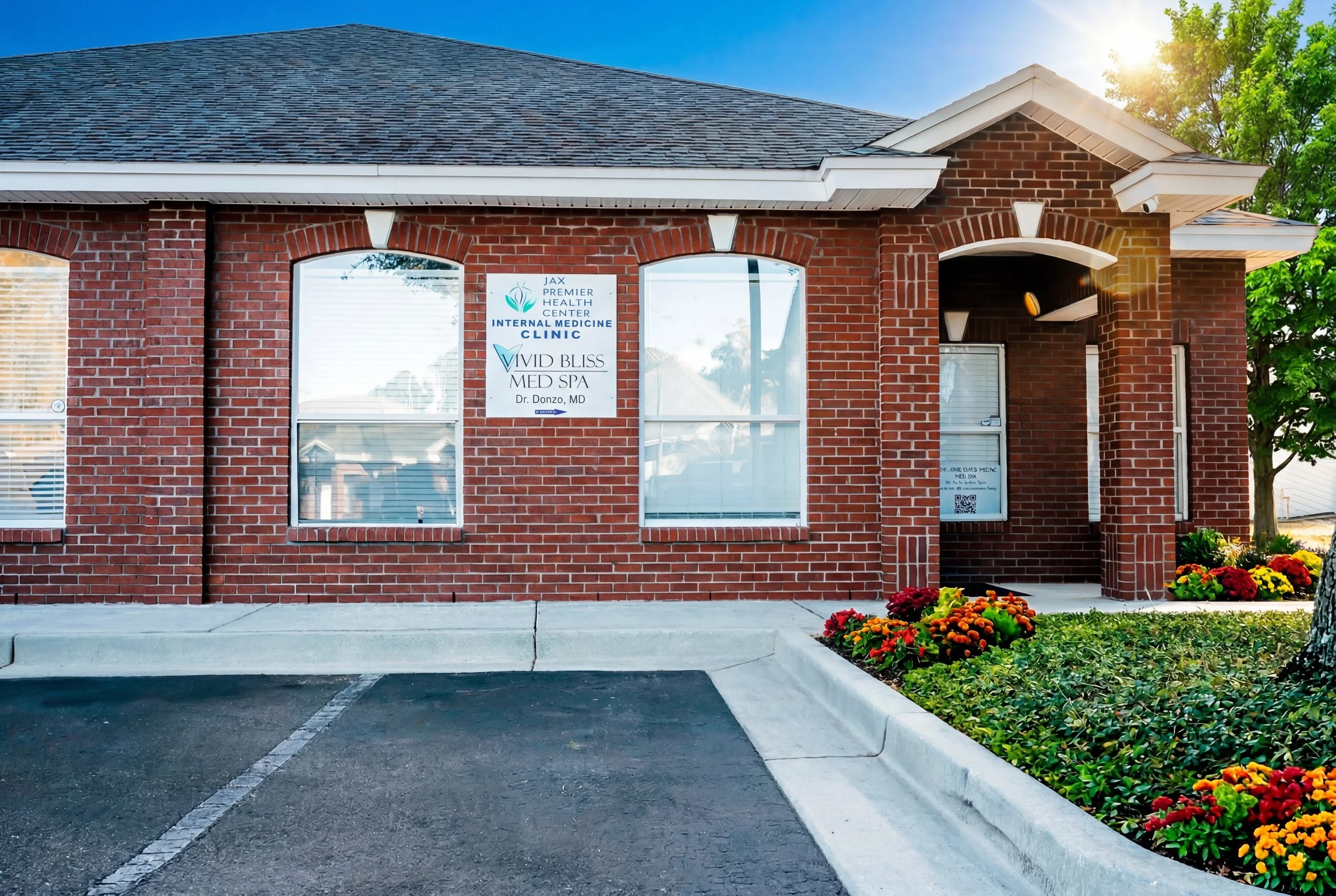 Exterior of a brick medical clinic building with a parking lot in front, flower bed with orange and yellow flowers, and a sign for JAX Premier Health Center, Internal Medicine Clinic, Dr. Donzo, MD.