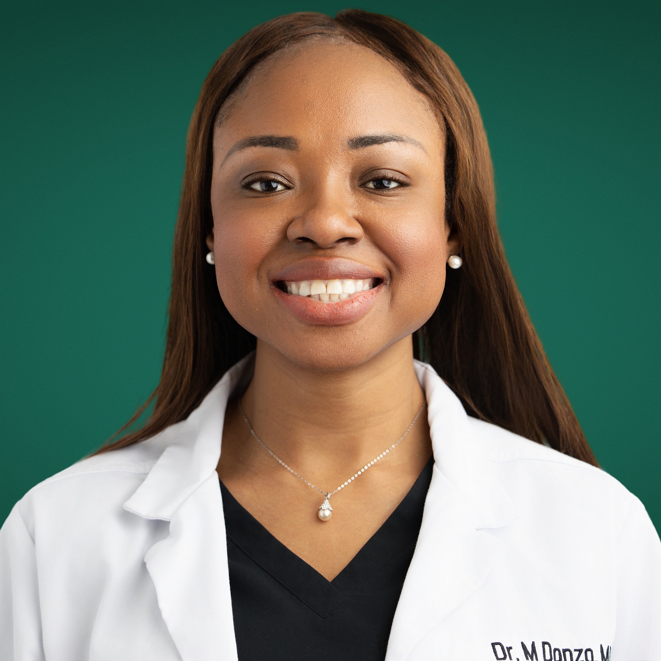 Close-up of a smiling African American woman wearing a white professional coat, pearl earrings, and a pearl necklace, with a green background.