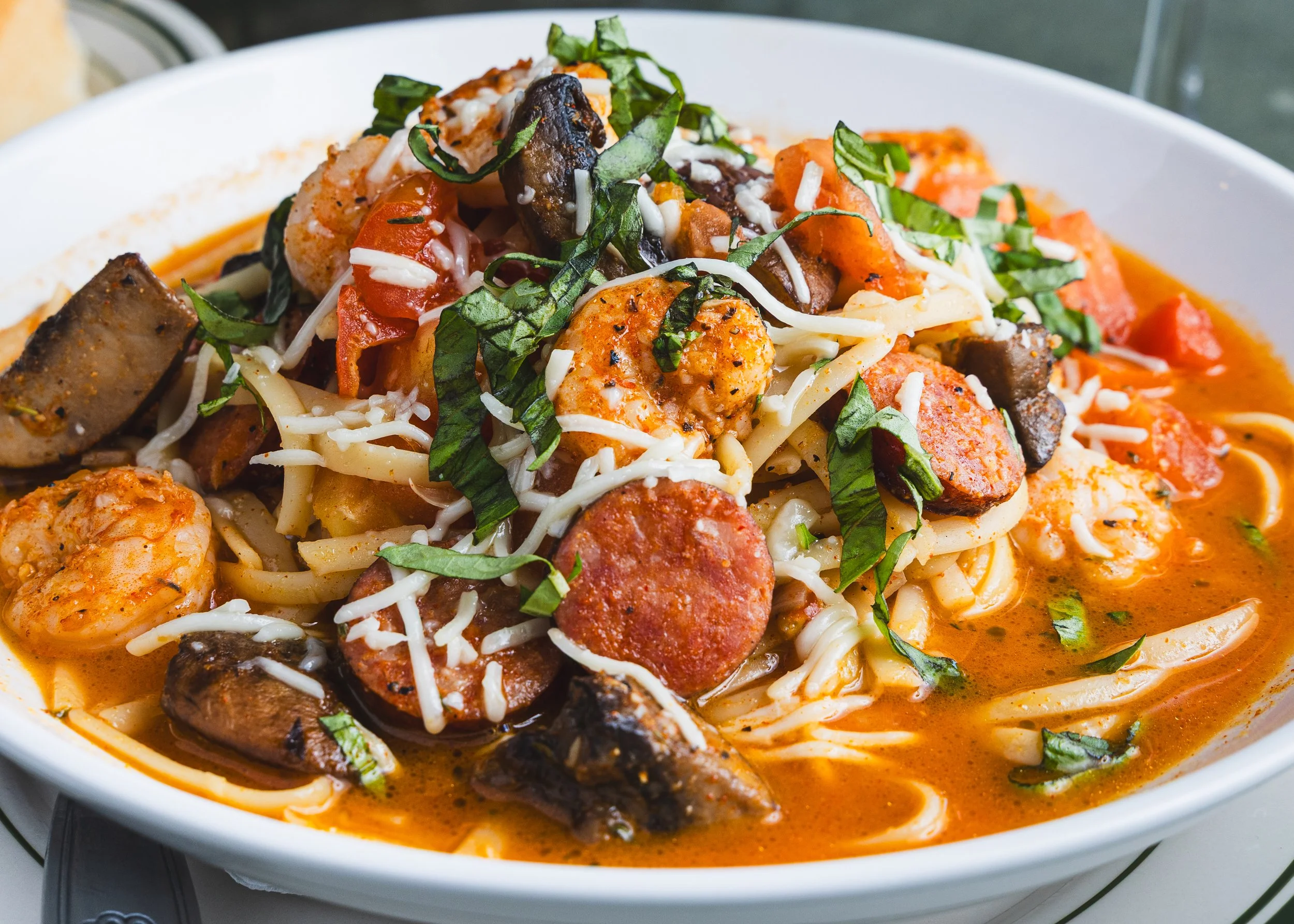 A bowl of pasta with shrimp, sausage, mushrooms, and chopped basil, in a creamy tomato sauce.