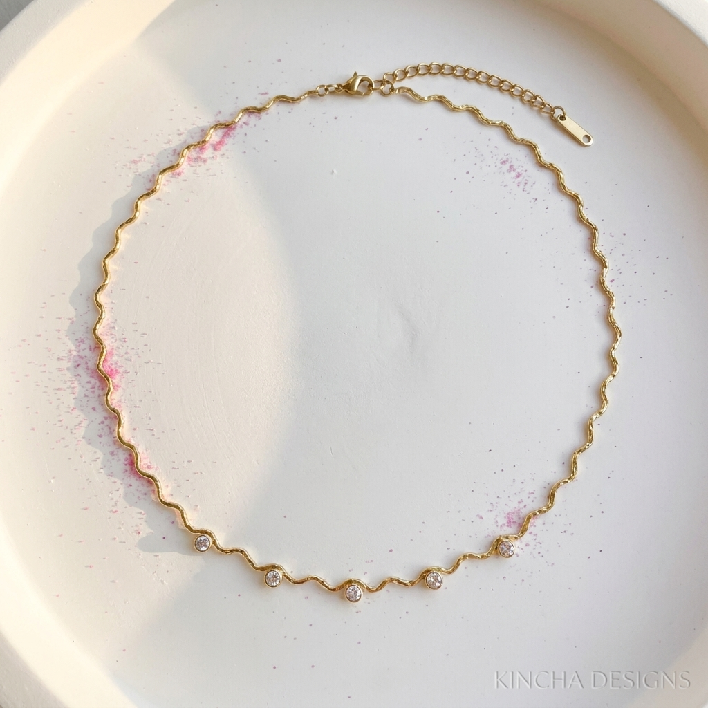 Gold crystal station wave chain necklace on white surface with fuchsia pink powder - stainless steel jewellery London - Kincha Designs