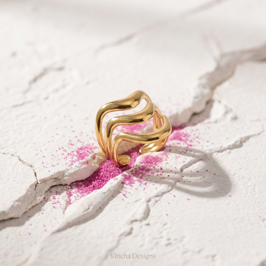 Gold wave ring close up on cracked stone with pink powder - waterproof jewellery - Kincha Designs