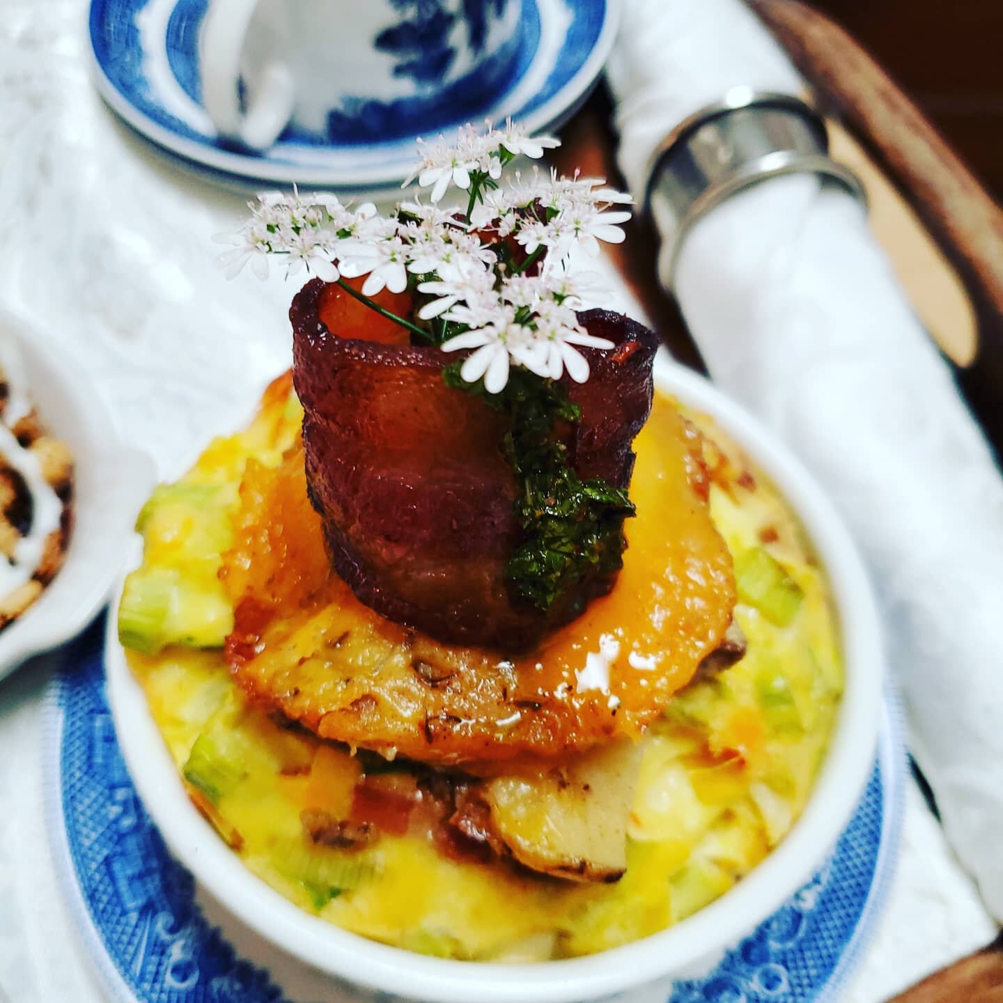 The American bacon breakfast: Eggs with sweet peppers, cream, bacon curl, cheddar scalloped potatoes, chimichurri and a cilantro flower....