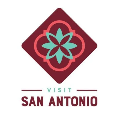 Logo with a teal and pink flower design inside a diamond shape with the text 'Visit San Antonio' below.