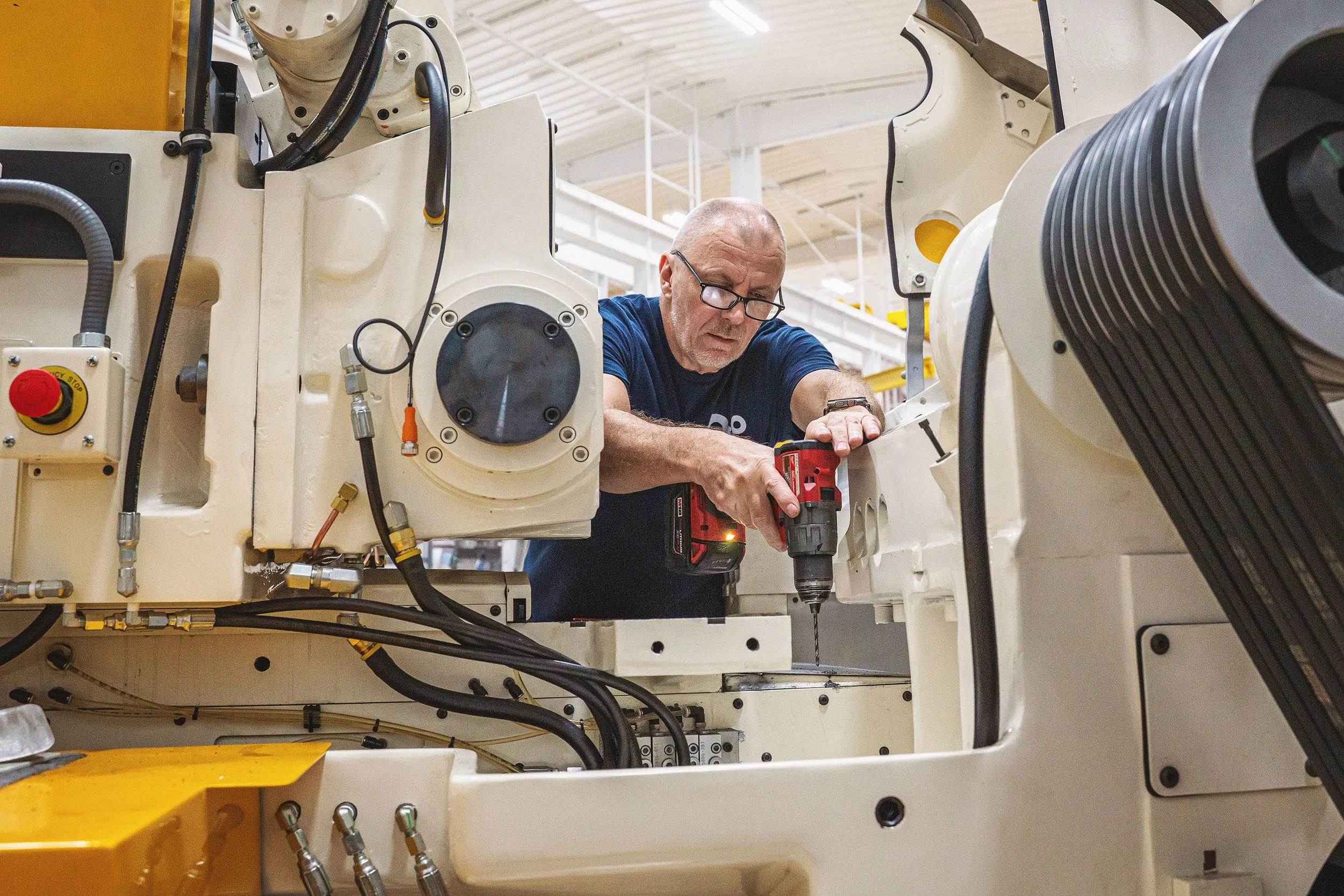 A man working inside a large industrial machine, using a power drill in a factory setting.