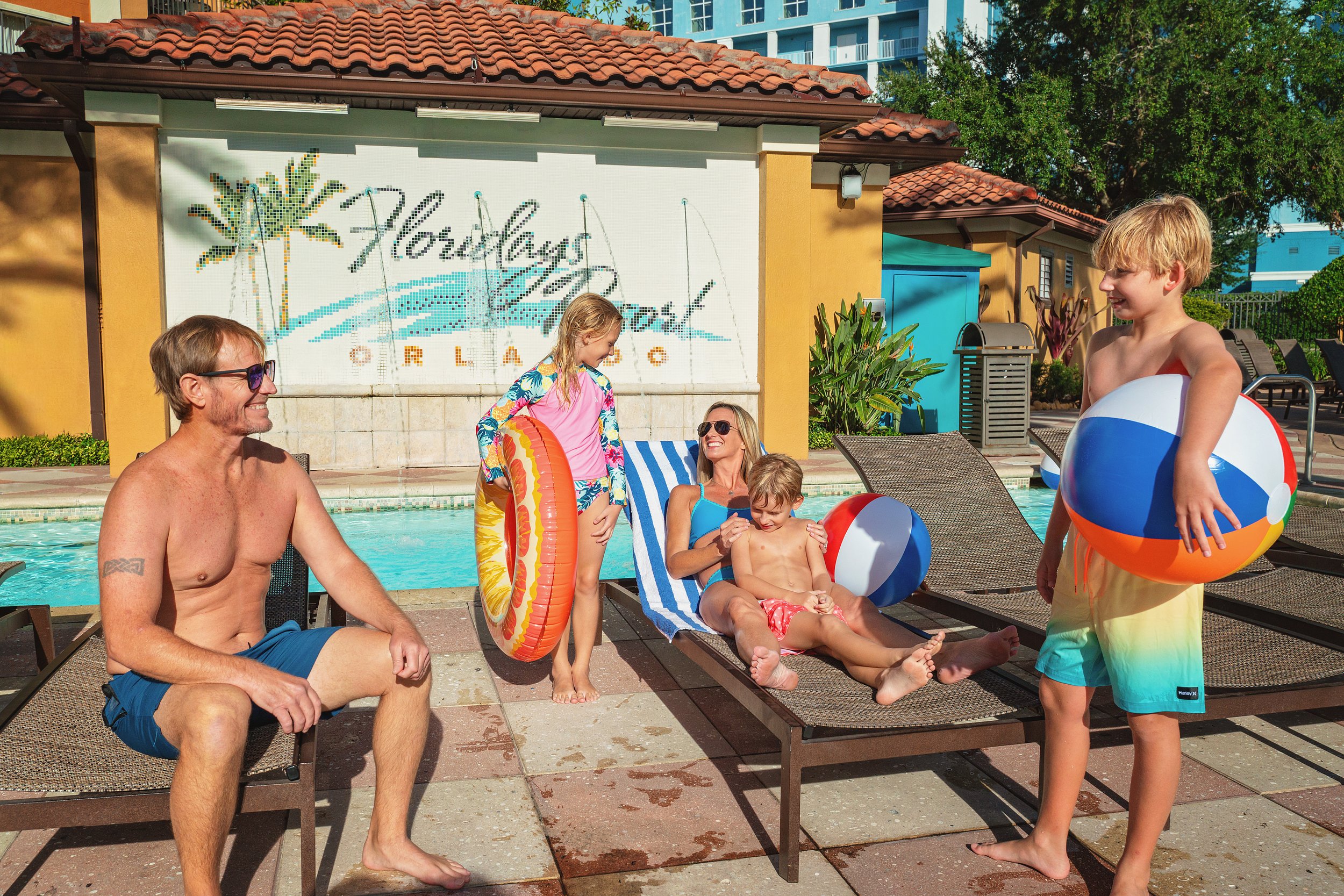 Family enjoying poolside fun at the Hard Rock Hotel Orlando, with children holding beach balls and adults sitting and lounging in swimwear.