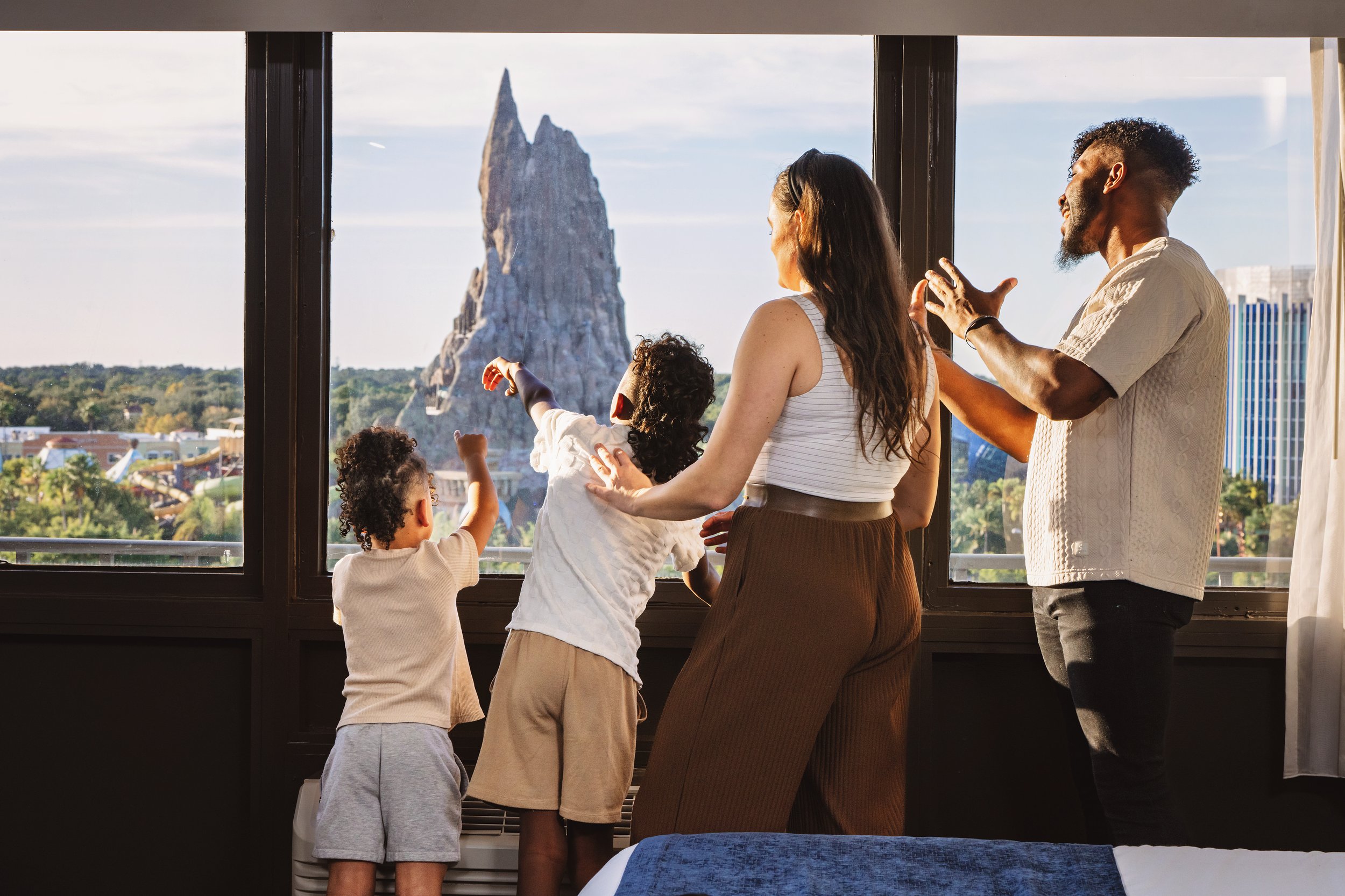 A family of five, including three children and two adults, inside a room with a large window showing the Tower of Terror ride at Disney California Adventure Park in the background.