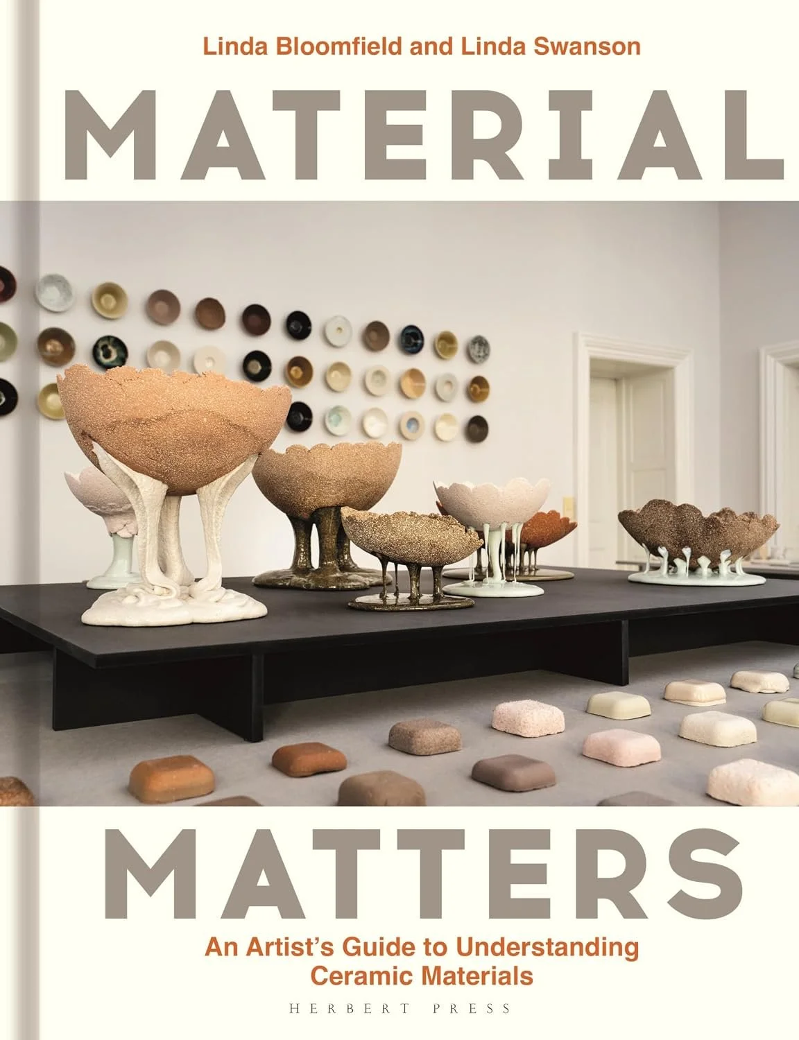 Material Matters: An Artist's Guide to Understanding Ceramic Materials cover image with clay pinch pots on a black plinth, test bars, and small bowls hung on the wall in a grid