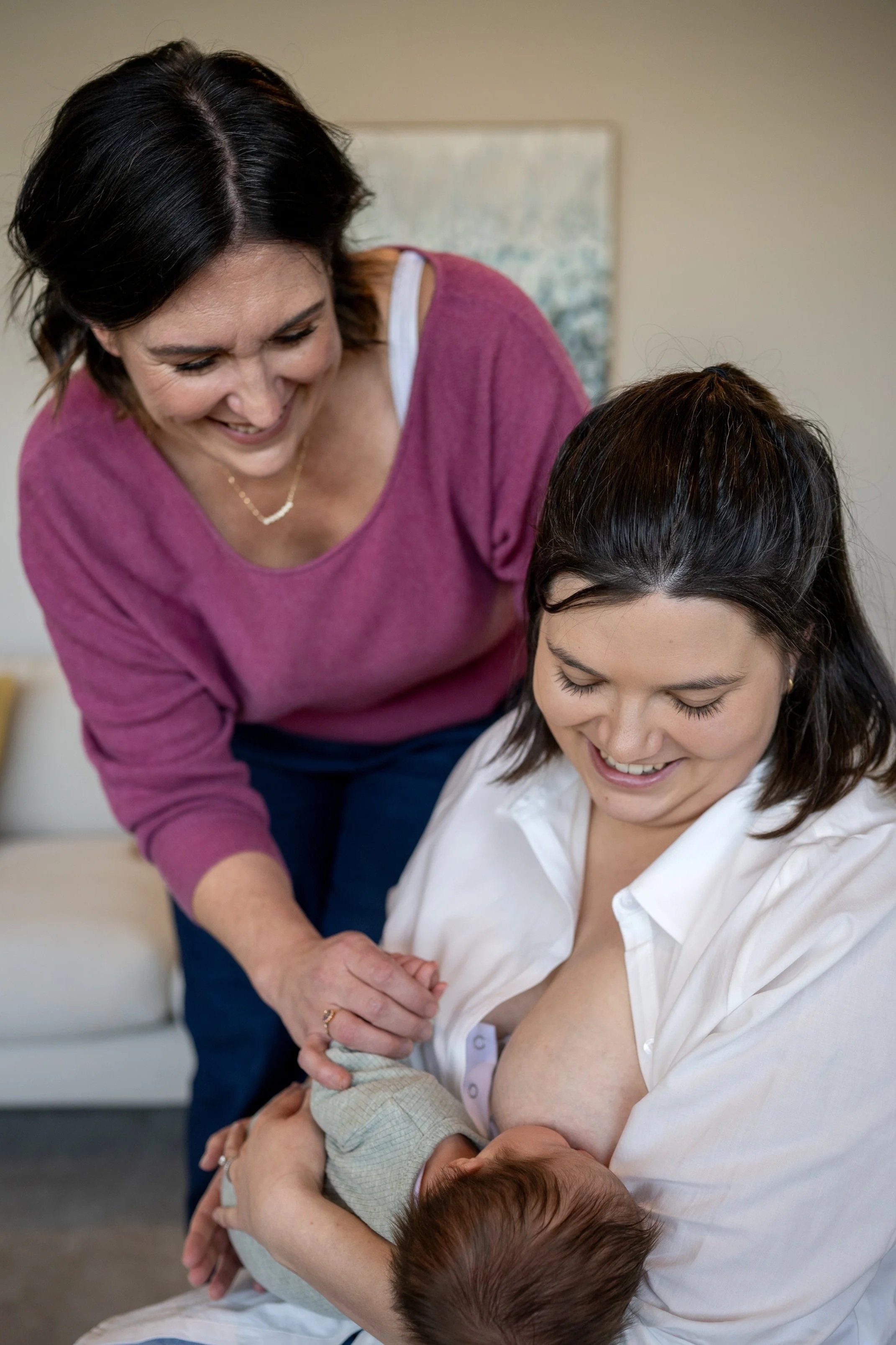 A woman breastfeeding a baby while Dr Amber Hart observes and provides support, inside our Maternal and Infant Wellbeing Melbourne Day Stay lounge.