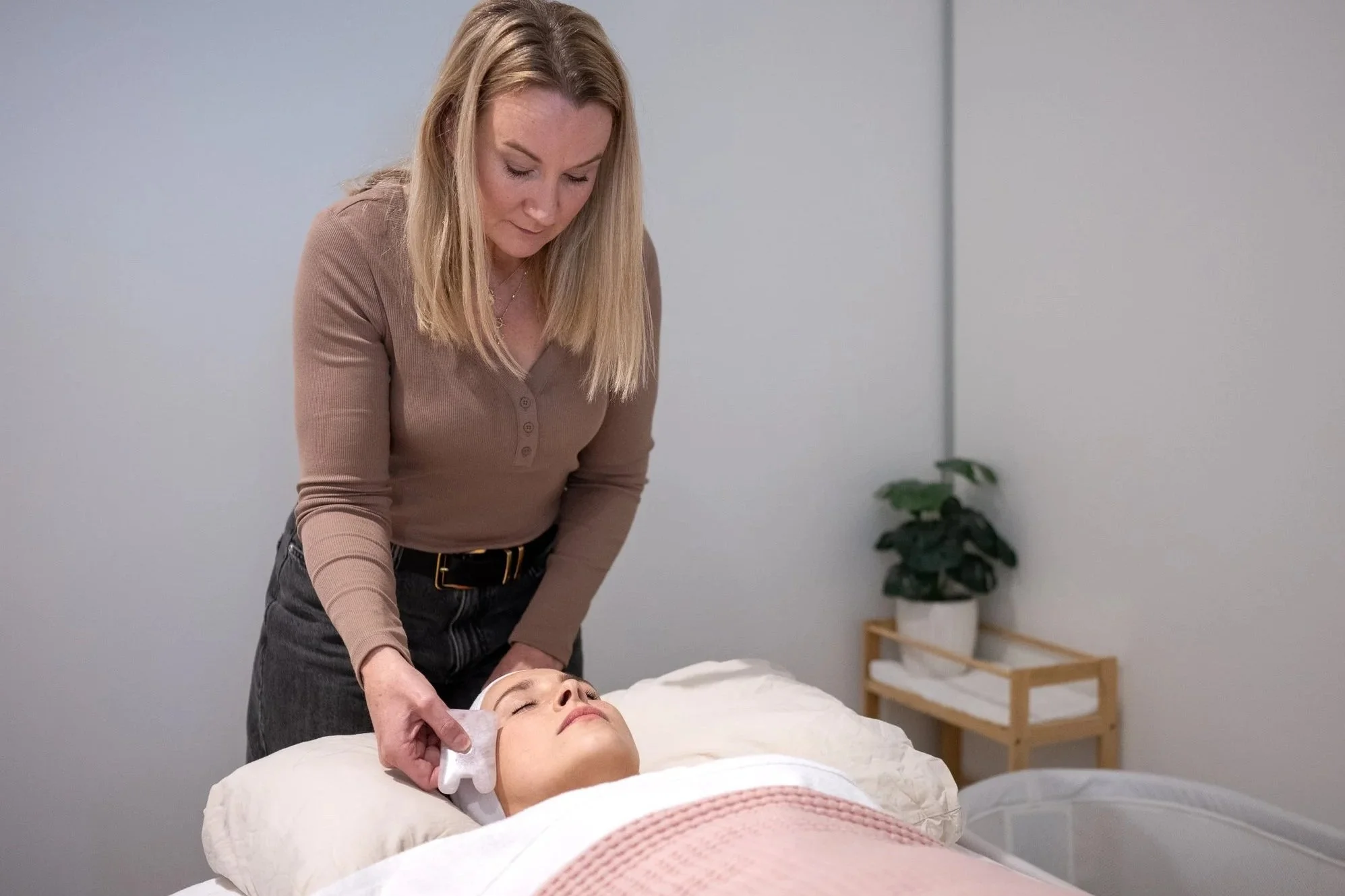 Nardia Saunders providing a facial treatment to a woman lying on a treatment bed in a Maternal and Infant Wellbeing Melbourne spa room.