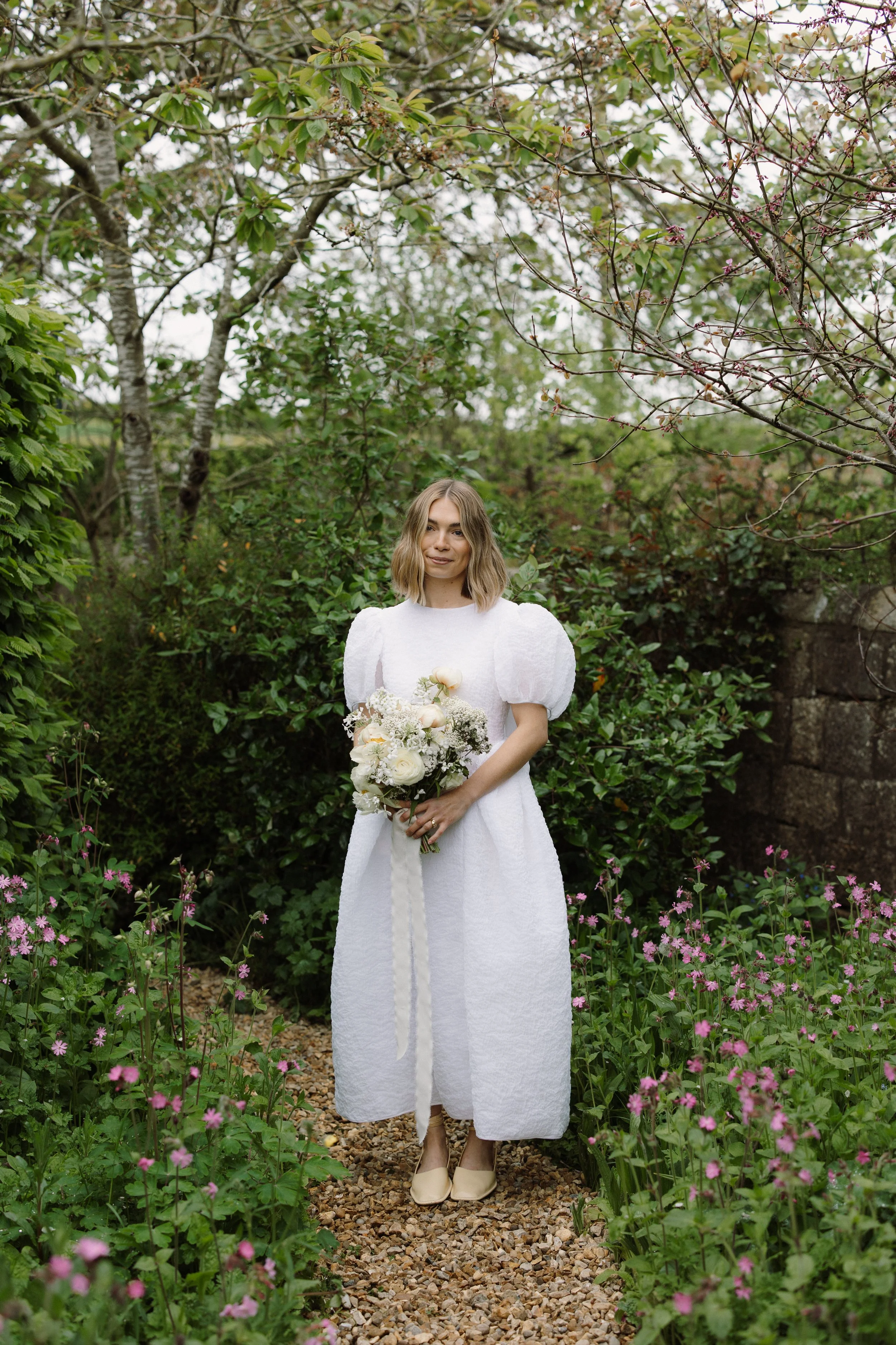 Bride wearing Cecilie Bahnsen and holding her honour farm flowers bespoke hand tied bridal bouquet made with seasonal flowers in the UK.