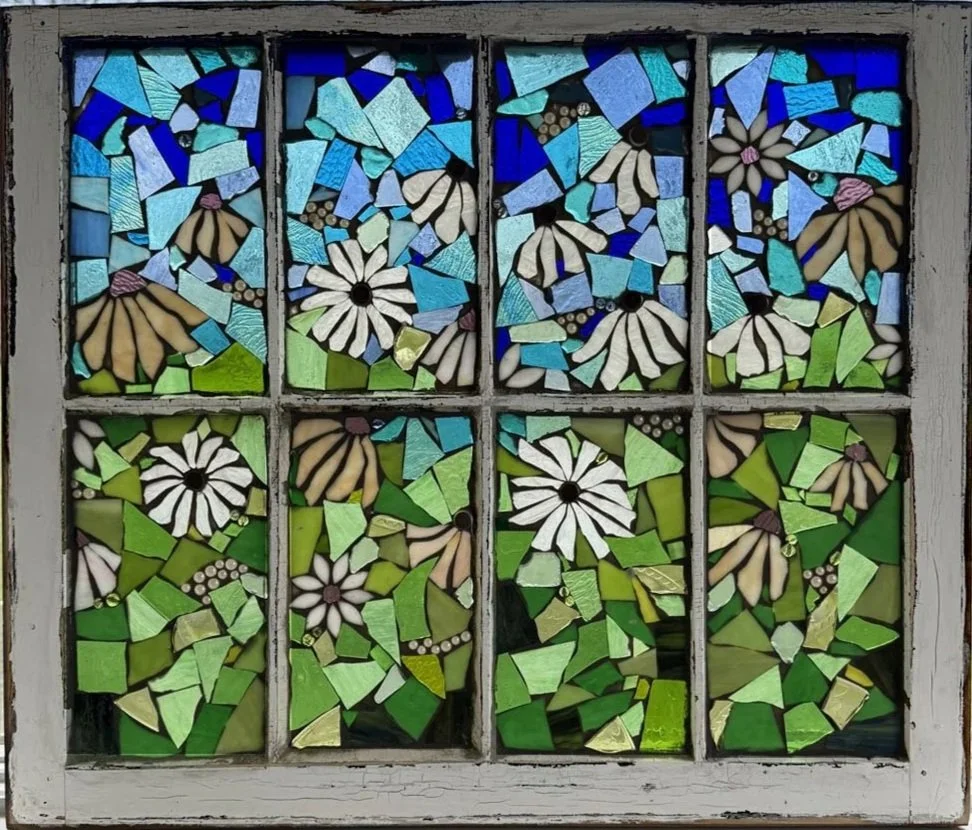 Colorful stained glass window featuring flowers and abstract shapes in shades of blue, green, and beige.