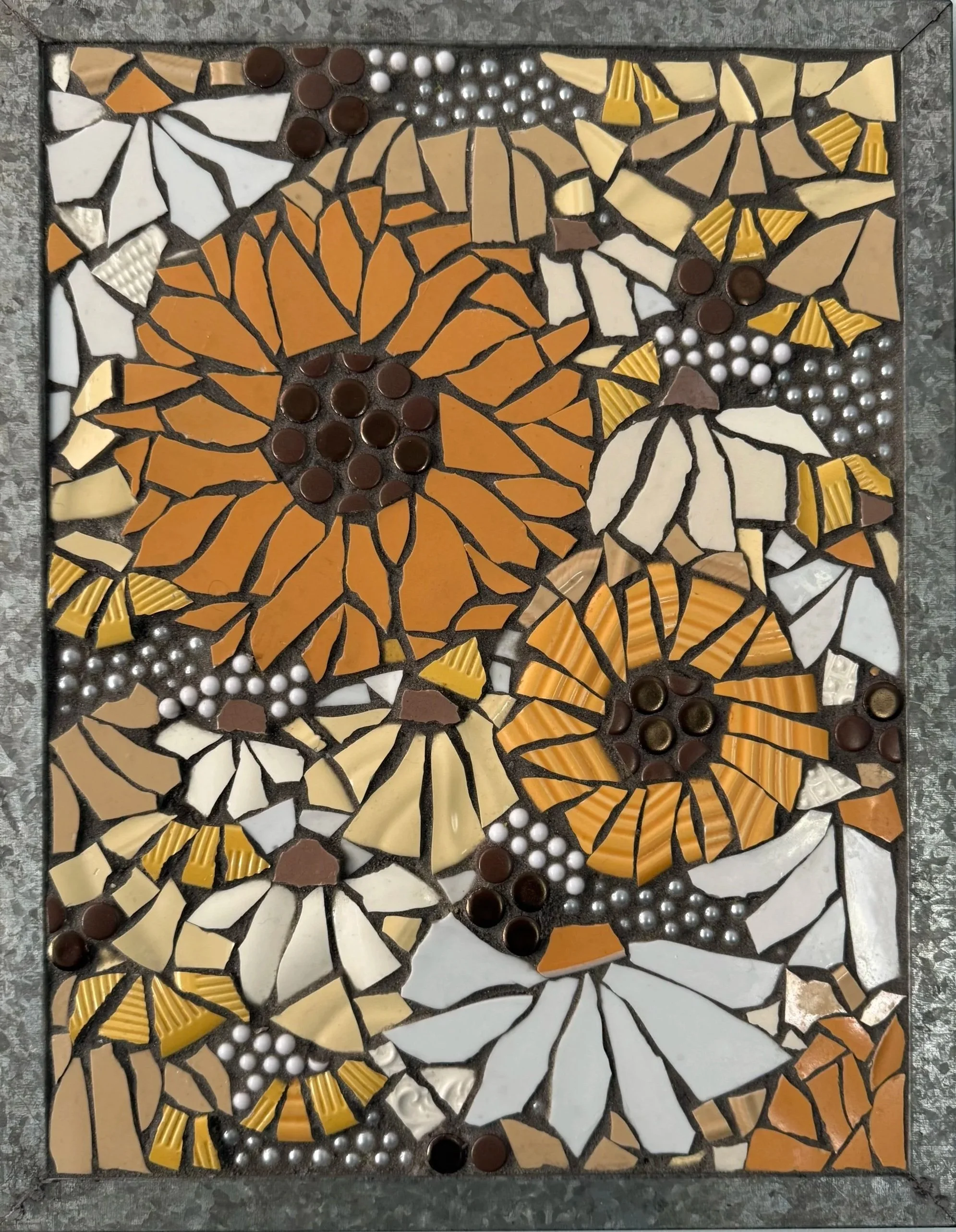 A decorative mosaic tile artwork featuring sunflower images with orange and yellow petals made from various shaped and colored tiles. The mosaic includes brown, white, pearl, and yellow tiles, arranged to depict the sunflower petals and centers with 
