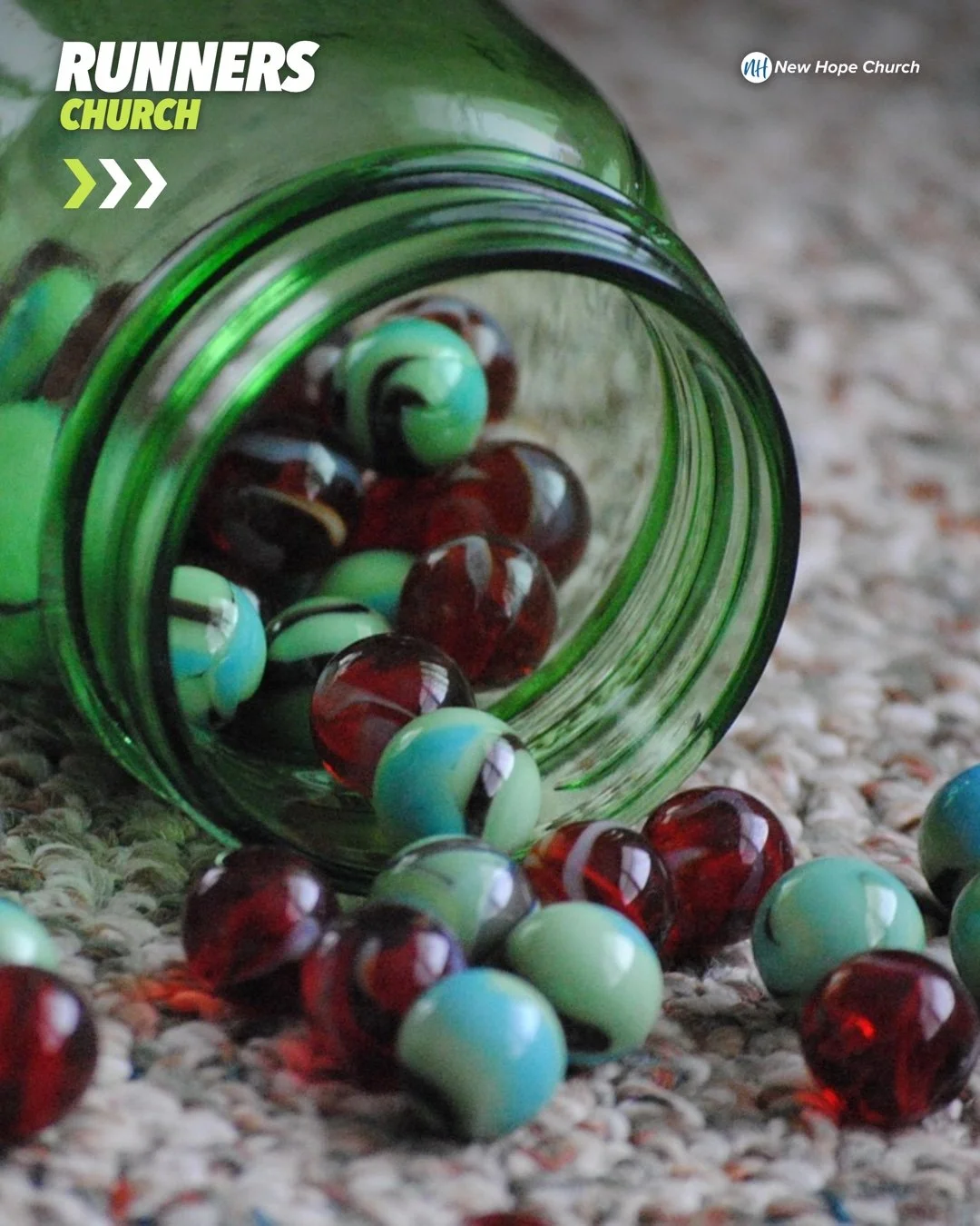 A green glass mason jar tipped on its side with red and turquoise marbles spilling out of the mouth onto the floor.