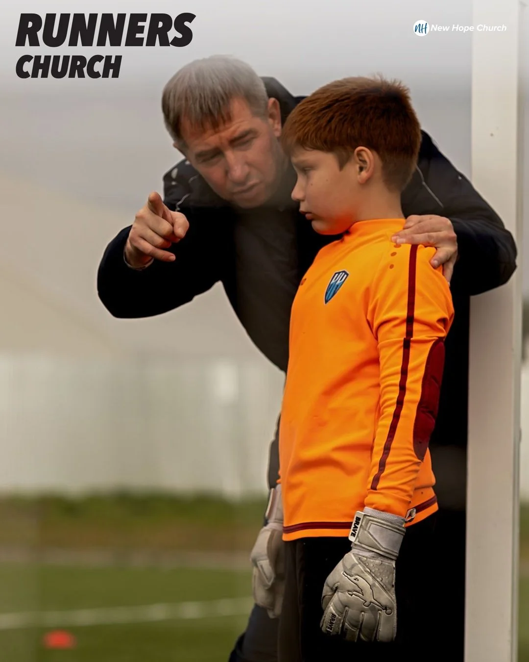 A soccer coach leaning over to guide a young goalkeeper beside the goal during practice.