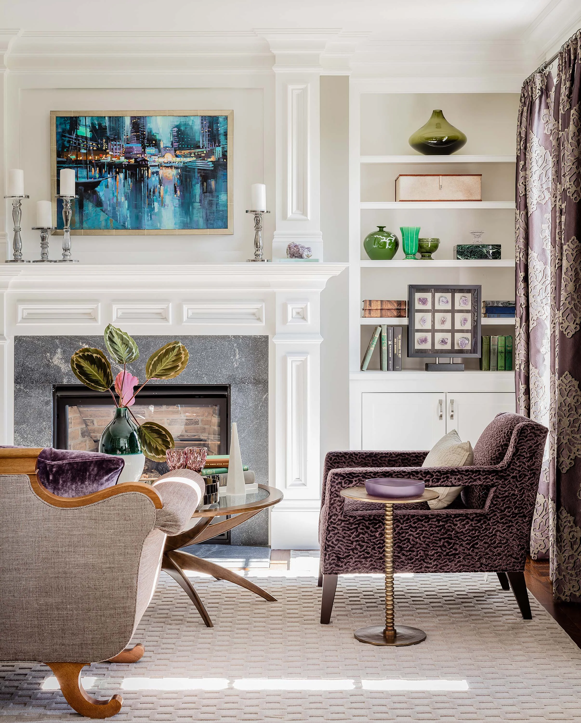 Living room with fireplace, printed armchair, white cabinet and round glass center table, mitchell gold bob williams, currey, curry and company, duke chair, custom rug, built in bookcase