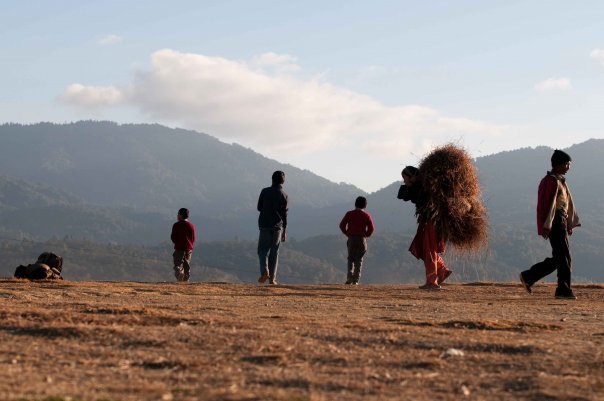 Children play football in the dust - women lug bales of hay.