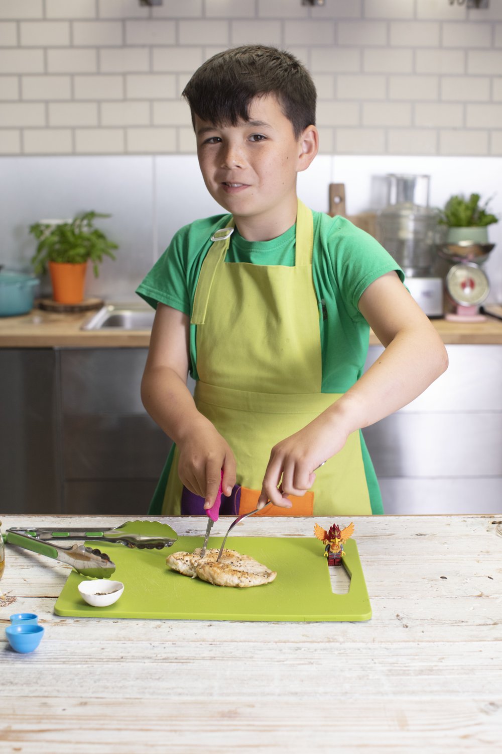 boy with green apron is slicing the bashed chicken