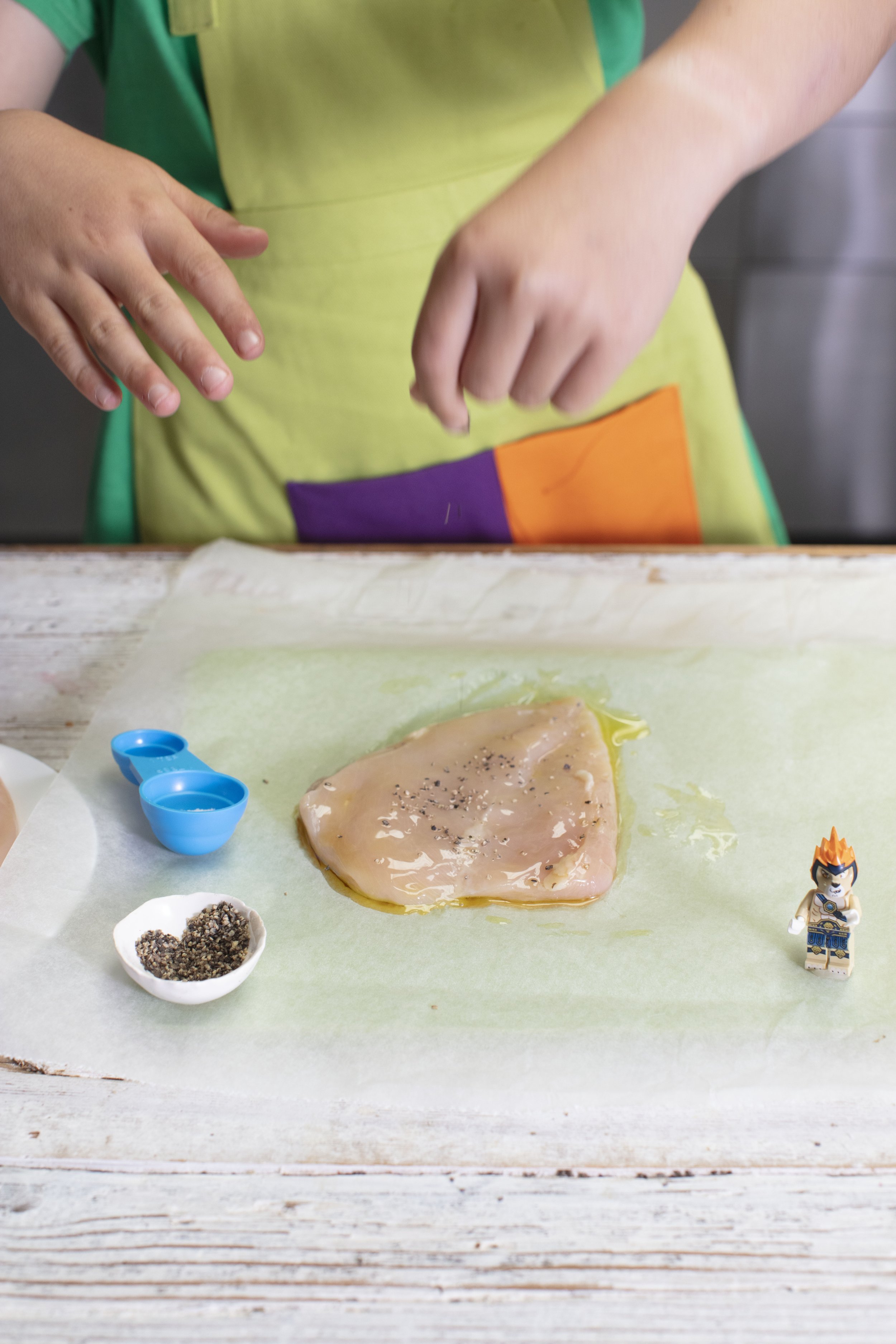 boy with green apron is seasoning the bashed chicken