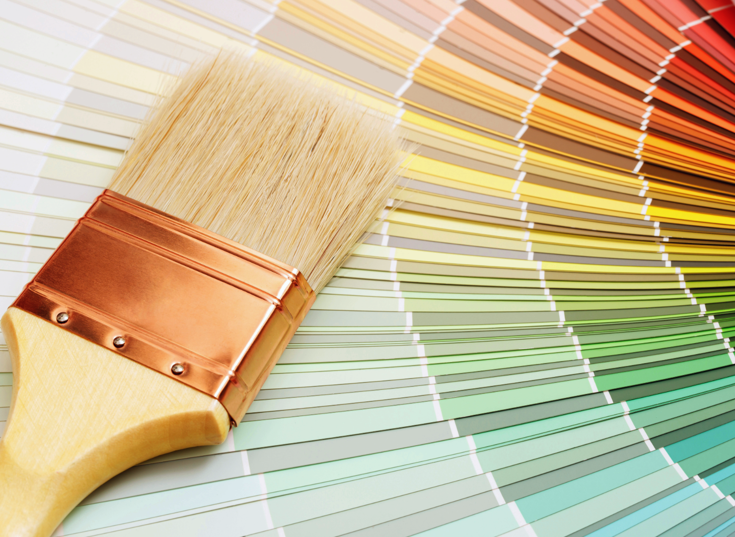A paint swatch fan deck with a paintbrush resting on top, showcasing a spectrum of colors from warm reds and oranges to cool greens and blues.