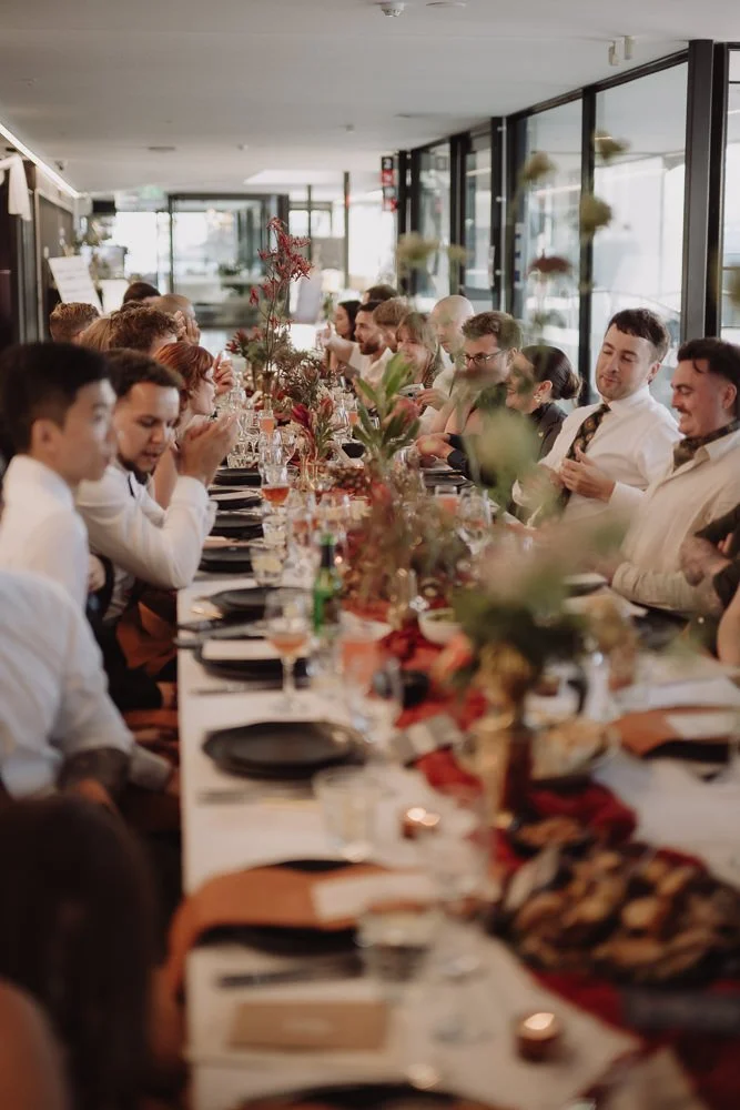 People gathered around a long dining table decorated with flowers and candles in a restaurant.