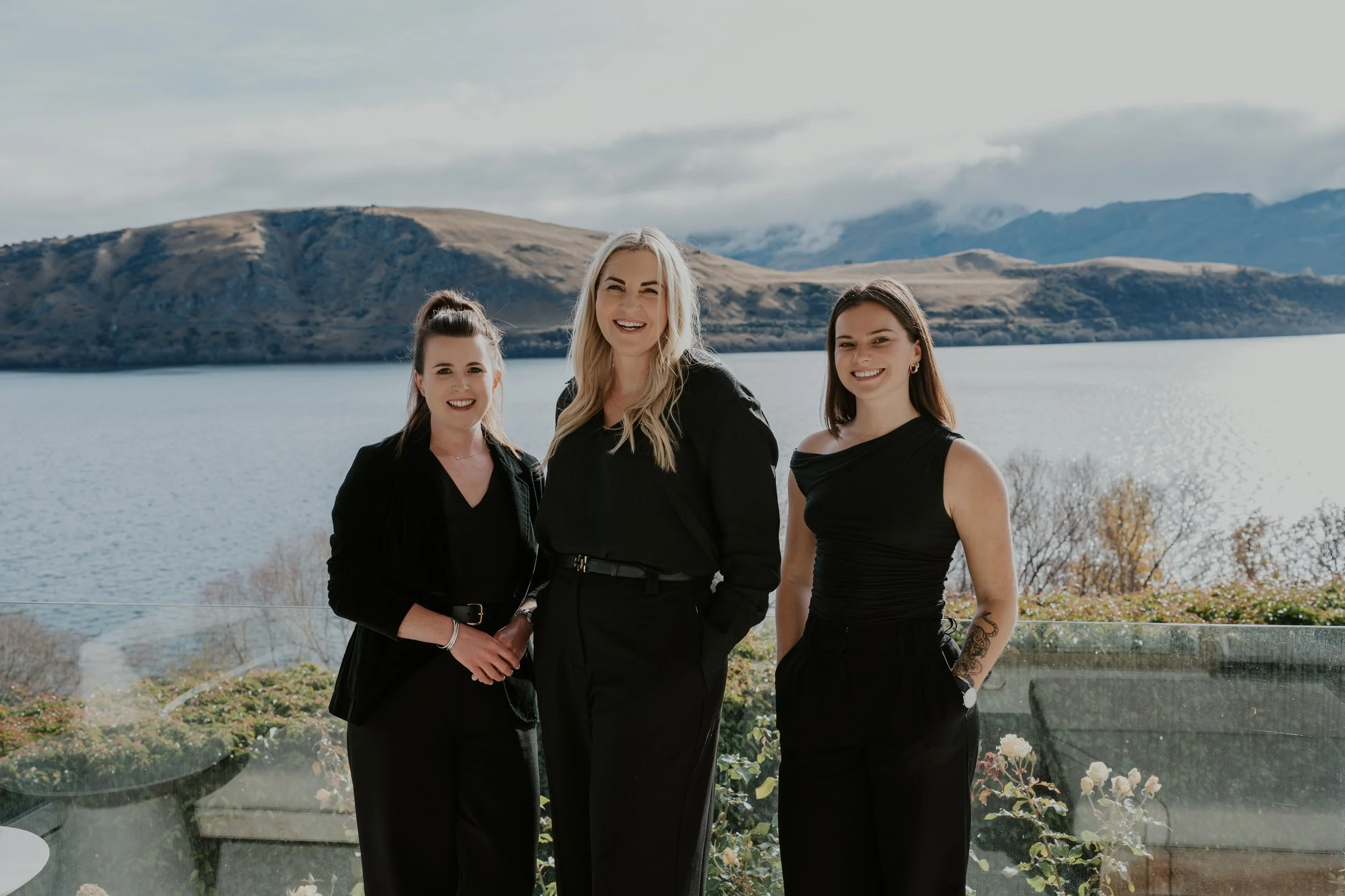 The Elite Management team dressed in black on a balcony overlooking Lake Hayes with hills in the background