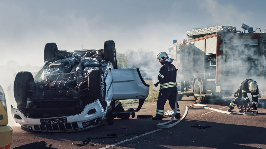 Firefighters putting out a fire on an overturned car.