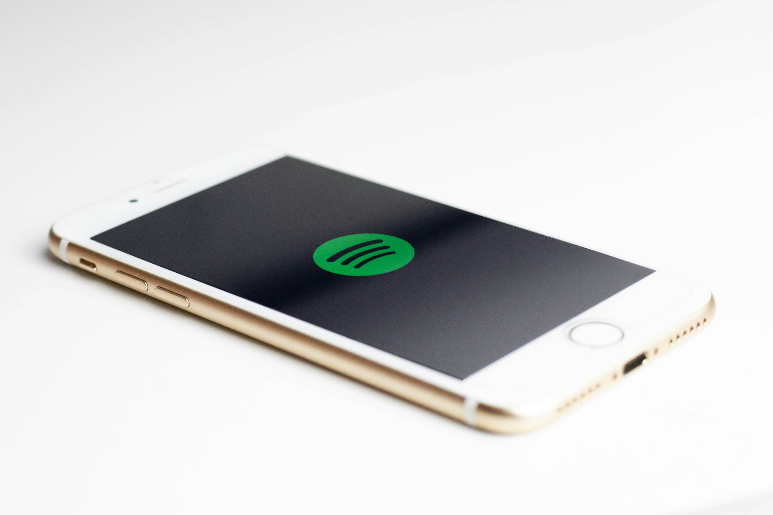 A white smartphone with a black screen displaying a green Spotify logo, placed on a white surface.