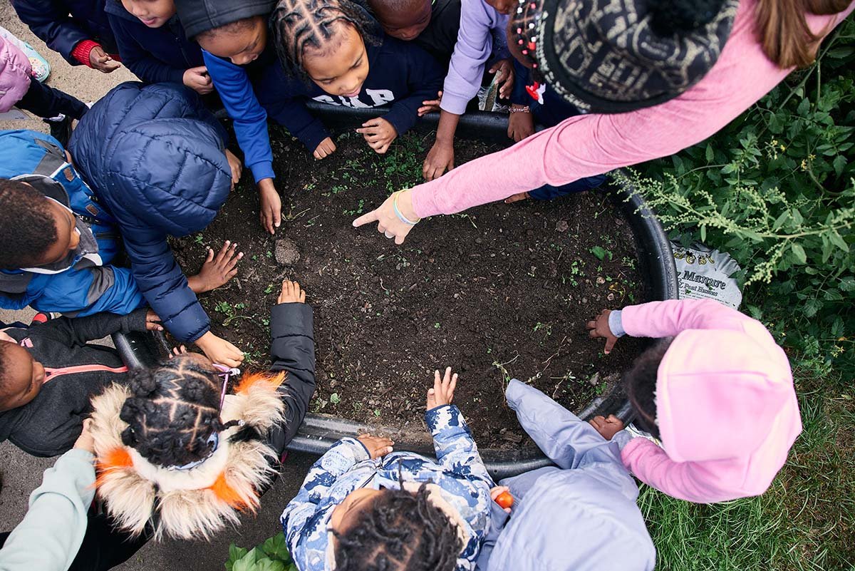Students at Bethune Early Childhood Development Center gather around a raised garden bed, excited to get their hands in the dirt and learn about fall seed planting.