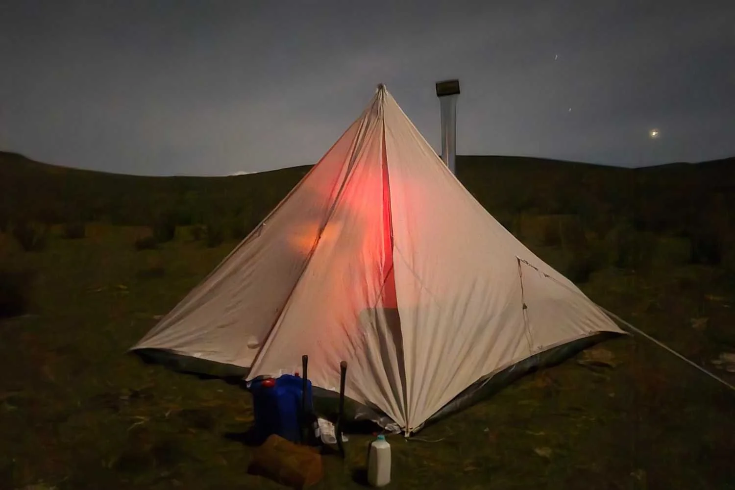 Canvas pyramid tent at night with stove pipe