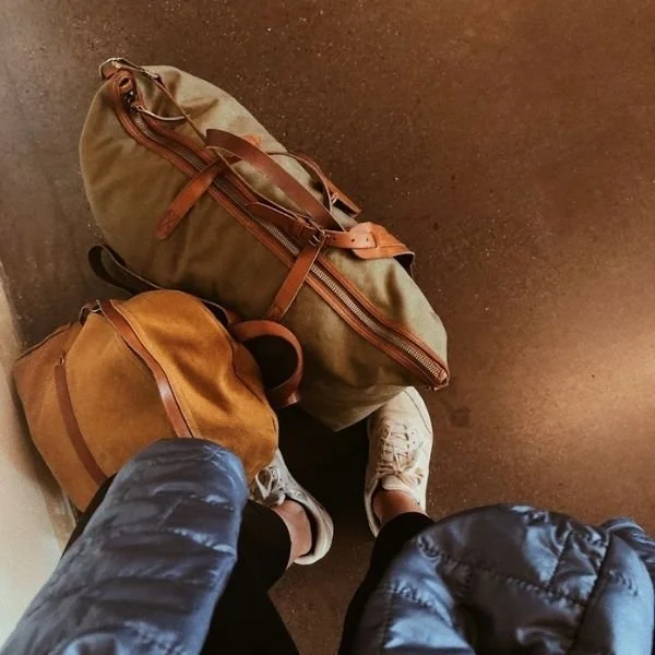 downward view of canvas duffel bag next to shoes of person traveling