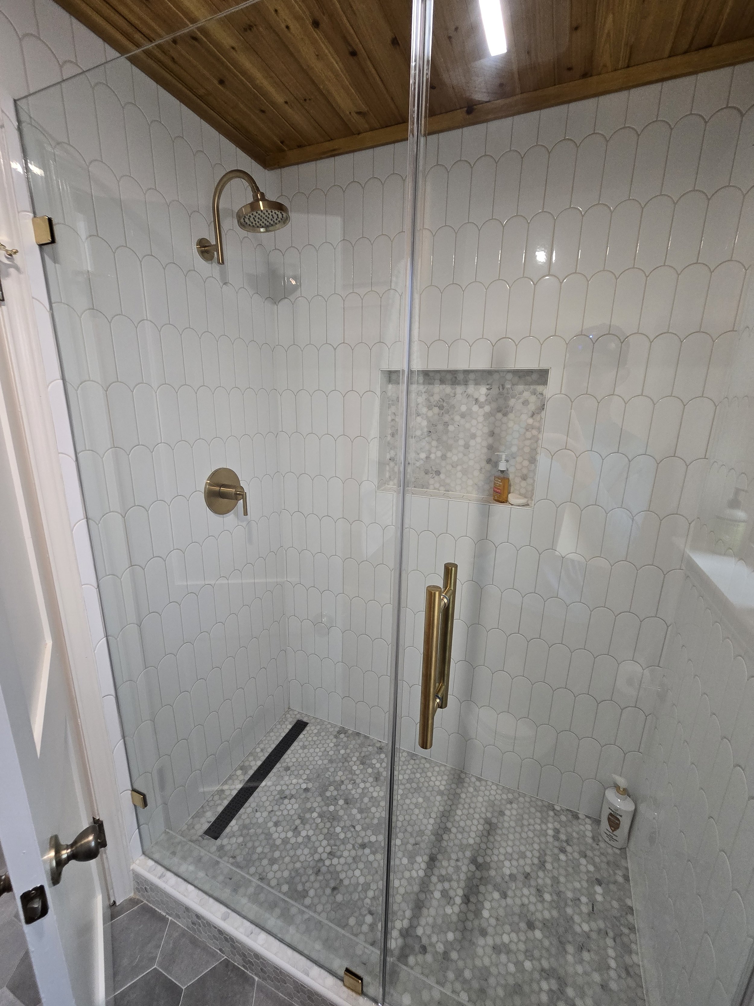 This is an image of a walk in shower with gold accessories, and white tile that has been replaced in clear lake