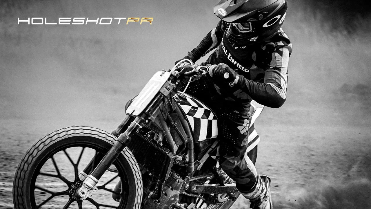 A Royal Enfeld motorcycle drifts in the dirt, photo features the Holehost motorcycle PR logo