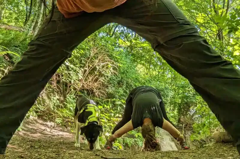 Adam frames a shot using his legs, with Chloe stretching with Dr. Heather on a forest path, symbolizing a personal commitment to a holistic and sustainable lifestyle that aligns with Ruff Day Vet's core philosophy.