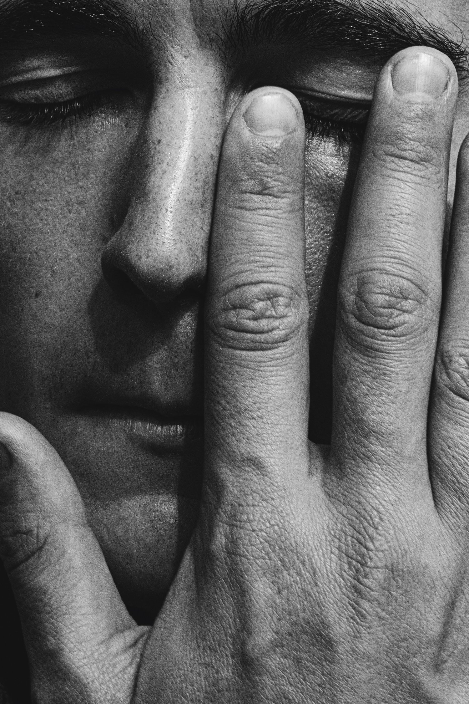 Black-and-white close-up of a person's eye and fingers pressing against the eyelid and cheek