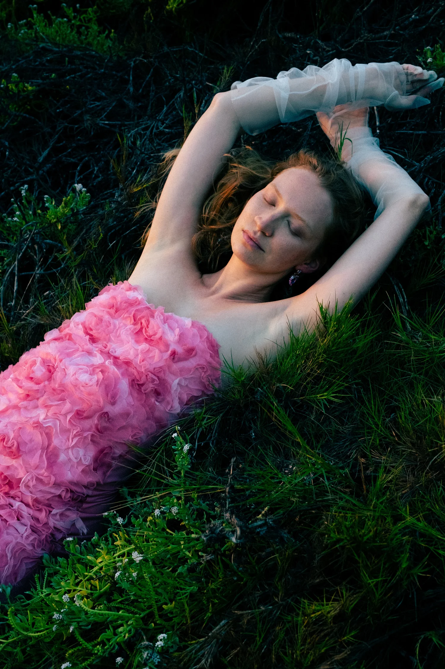 Woman in a sheer white dress lying in grass beside a large pink flower