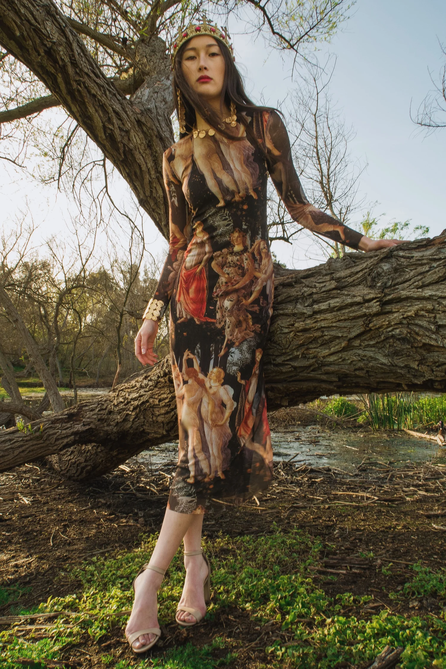 Woman wearing a floral crown and flowing patterned dress standing beside a large tree outdoors