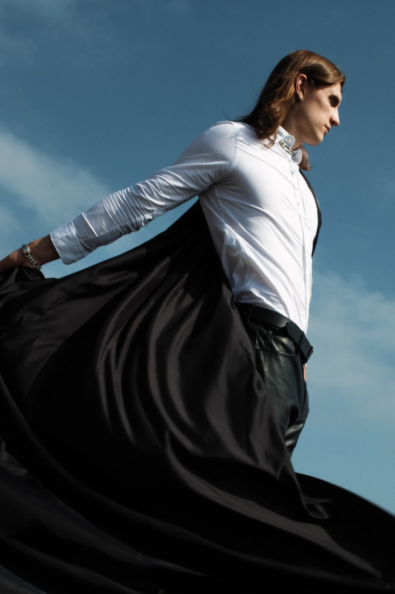 Man in a white blouse and flowing black skirt posing against a blue sky
