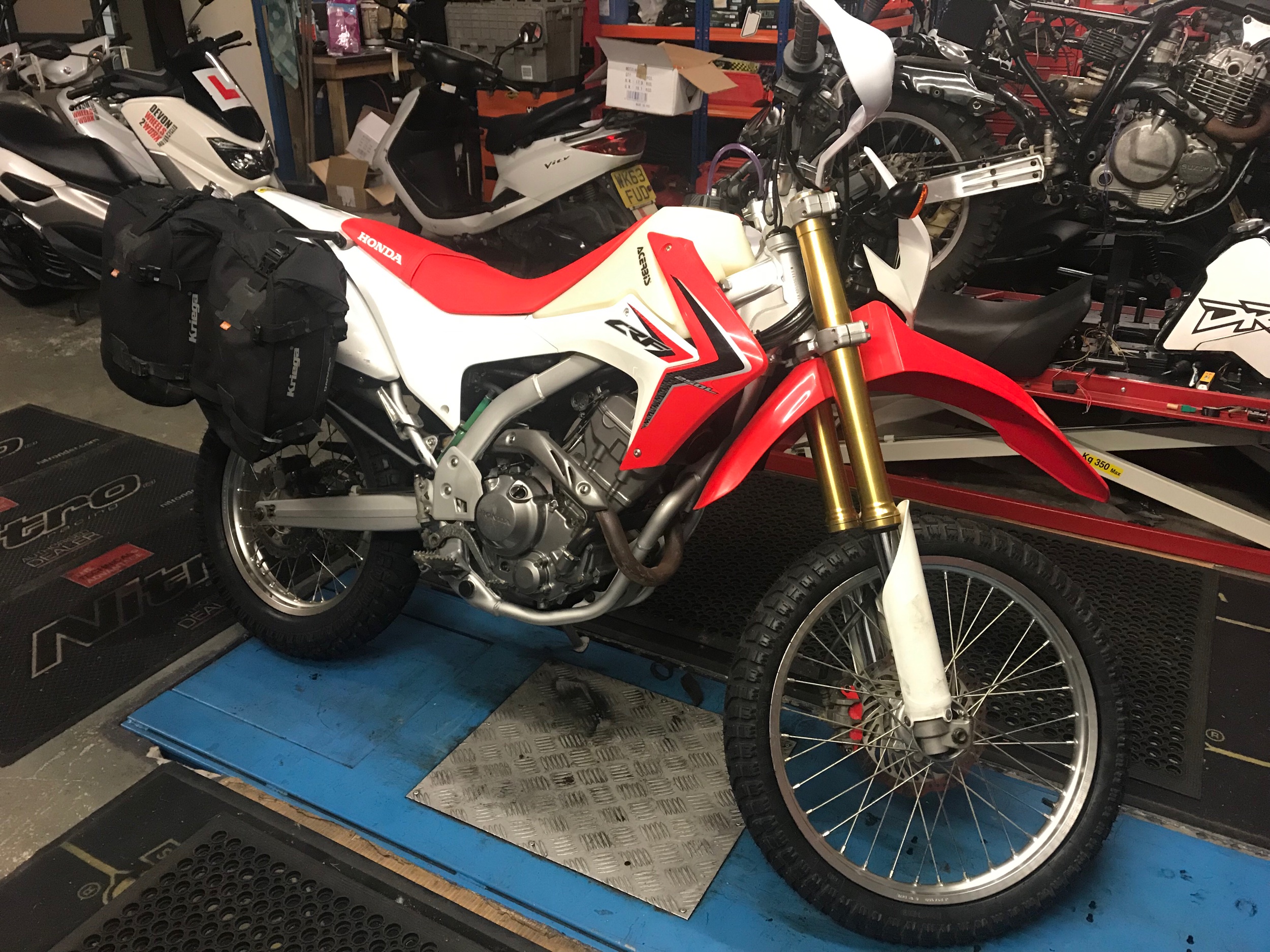 The CRF is still on the bench gaining mods as the days roll on! Latest additions are new boots, I chose Mitas E07’s as I used these on my last adventure to Albania on the KTM690, I was really pleased with both their wear and performance so I’m sticking with what I know for now. They are a good solid tyre that work well for me. The front tyre was an absolute pig to fit and I have a tyre machine! But it’s gone on well with a new front tube, the original one had been repaired and had a little damage so it was a no brainer to change it. The rear tyre was a lot easier to fit and I decided to keep the original heavy duty tube as it was in great condition. Both sets of wheel bearings were inspected at this point, they are in very good condition so I left them as they are noting the bearing numbers, I will carry spares as a precaution. Original bearings re-greased with ACF50 Corrosion Block grease and plenty behind the seals to try and keep the bearings in good order. I also fitted a USB charge port, I decided to buy an Interphone unit which are quite expensive but they last and are suited to the conditions. I’m about to experience, you can save a little cash buying a cheap Chinese copy but they do and will fail, I hate throwaway, so it’s best to pay a little more and get Proven components that actually work, especially when it comes to leky stuff. I have some of these in stock now so if you need one…. I decided to wire it to switched live and chose the low beam supply, cut and soldered in making sure the solder flux was cleaned off before Re-wrapping the loom, a good strong connection which should be fine for the whole journey. I must confess I hate electrics and don’t really feel comfortable doing this stuff but this mod is simple so I had a go and it worked out well. The next in the list is an external power supply for my homemade mini compressor, I need this if I have to inflate my, or indeed anyone else’s tyres, a simple Optimate plug wired straight to the battery with the plug accessible and tucked away under the tank. I bought a new Ram Mount which will give a good secure platform for my IPhone, that’s also been fitted and sits well on the left side of the bars so I’m IPhone ready now! A new quick fit clip mount for my Garmin 64S handheld GPS pretty much completes the work on the bars, just waiting for the Garmin Africa maps chip to arrive now. K&N washable air filter also arrived today, this will allow me to clean my air filter without having to worry about finding replacement filters, they are expensive but I feel they represent good value in the long term. That’s nestled in the air box ready for action, a simple mod and a very worthwhile investment. I ordered a couple of new spark plugs, fitted one and the other added to the spares list, (boy were those expensive) I also chose to replace the plug cap as the old one was a little too loose for my liking. Next to come is the high screen and skid plate but they haven’t arrived yet. Booked her in for MOT just before the Adventure Overland Show in late September so I can leave with a fresh ticket. Prep feels like it’s going well, still haven’t really ridden the bike but I’m sure it will all fall into place, sitting in the bike it feels like a nice place to put down some miles, I will just have to get used to a little less power!! Happy days, Max