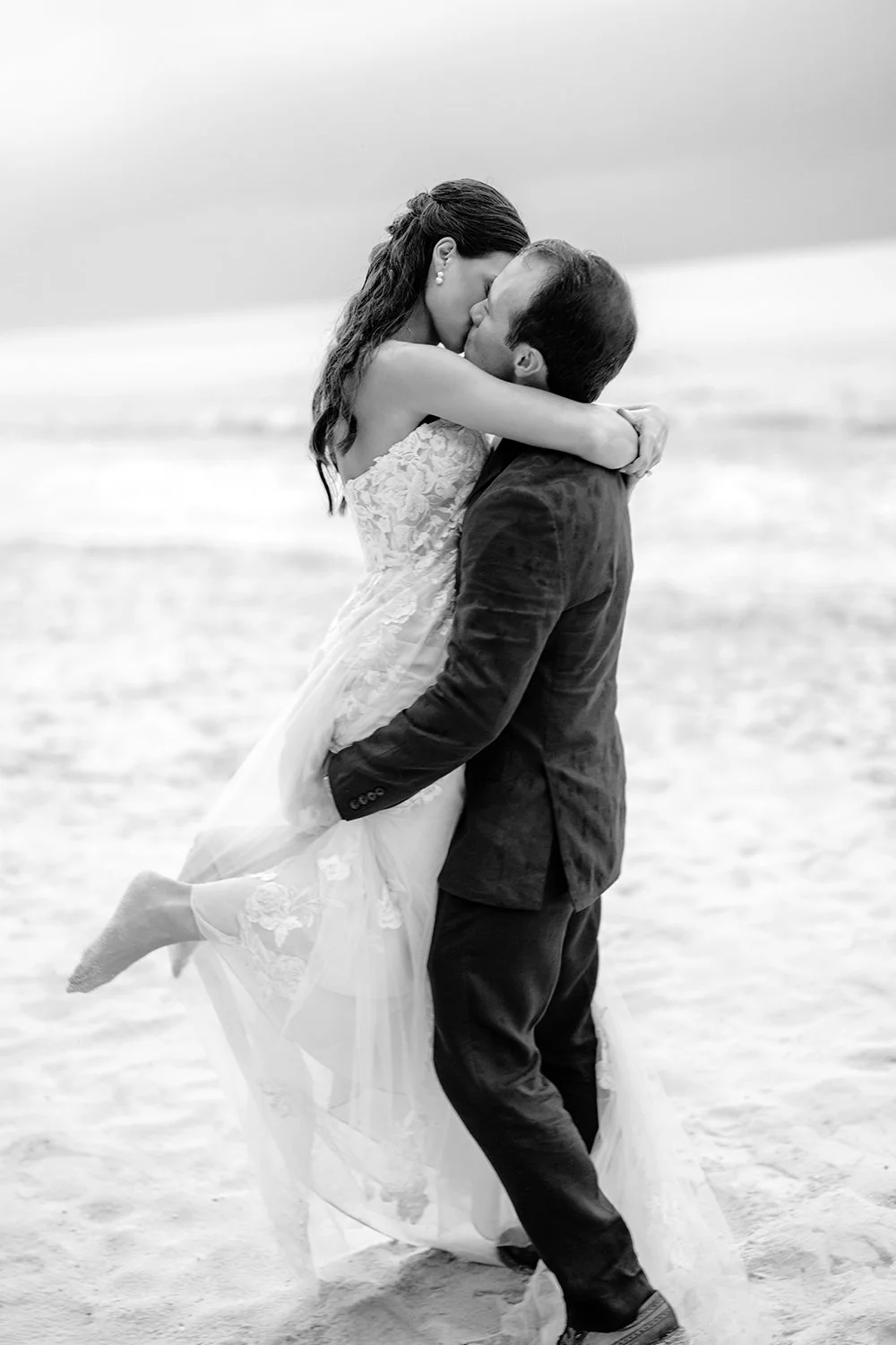43 Artistic photo of bride and groom kissing carrying the bride holding and hugging on the beach in a rainy day in cancun.jpg