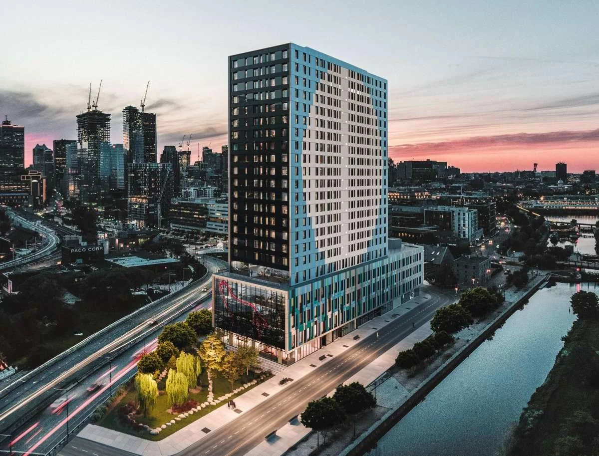 A modern high-rise building in an urban cityscape at sunset, with a river and city skyline in the background.
