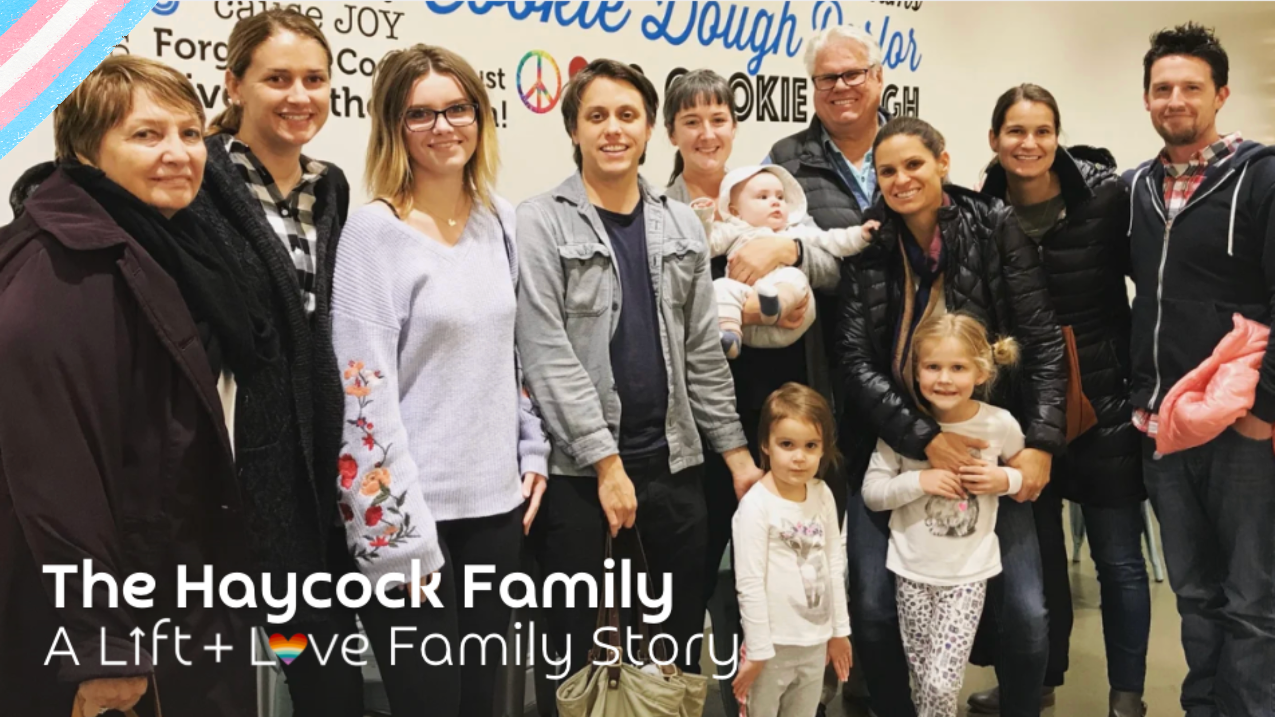 The Haycock family is gathered together indoors, smiling for a group photo. There are adults, children, and babies, with colorful decorations in the background, including words like 'joy' and 'peace.' The photo is captioned 'The Haycock Family: A Lift + Love Family Story.'