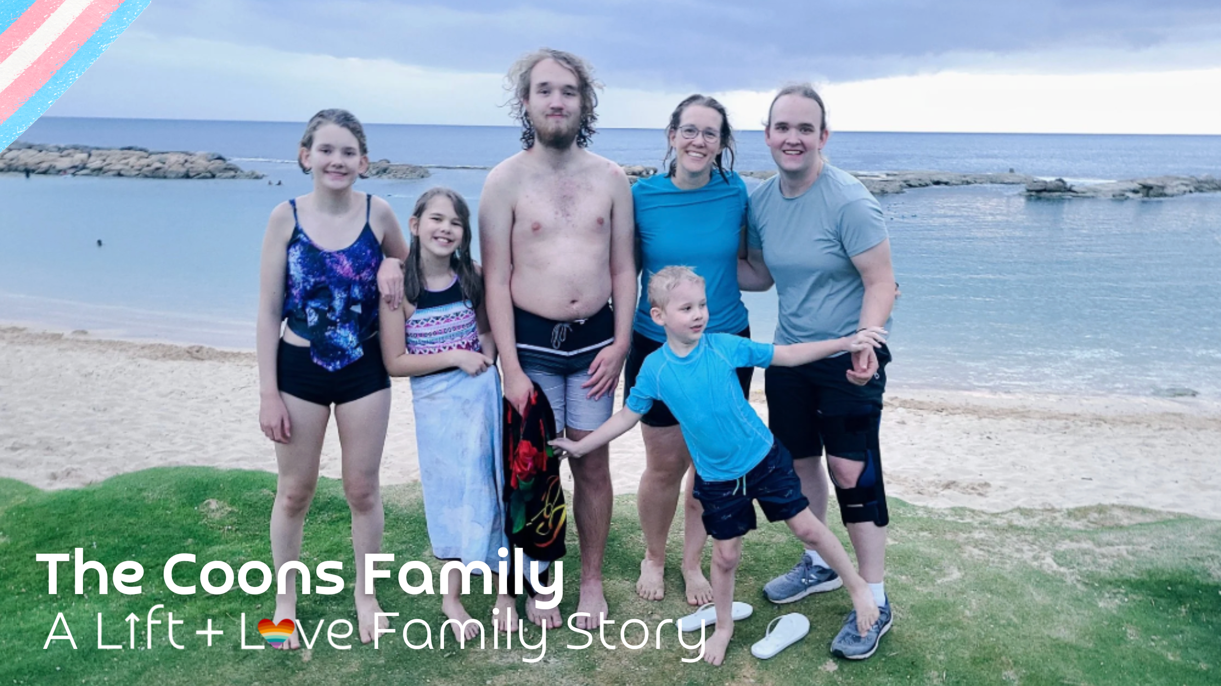 A family of seven standing on a grassy area near a beach, with the ocean and cloudy sky in the background, smiling at the camera.