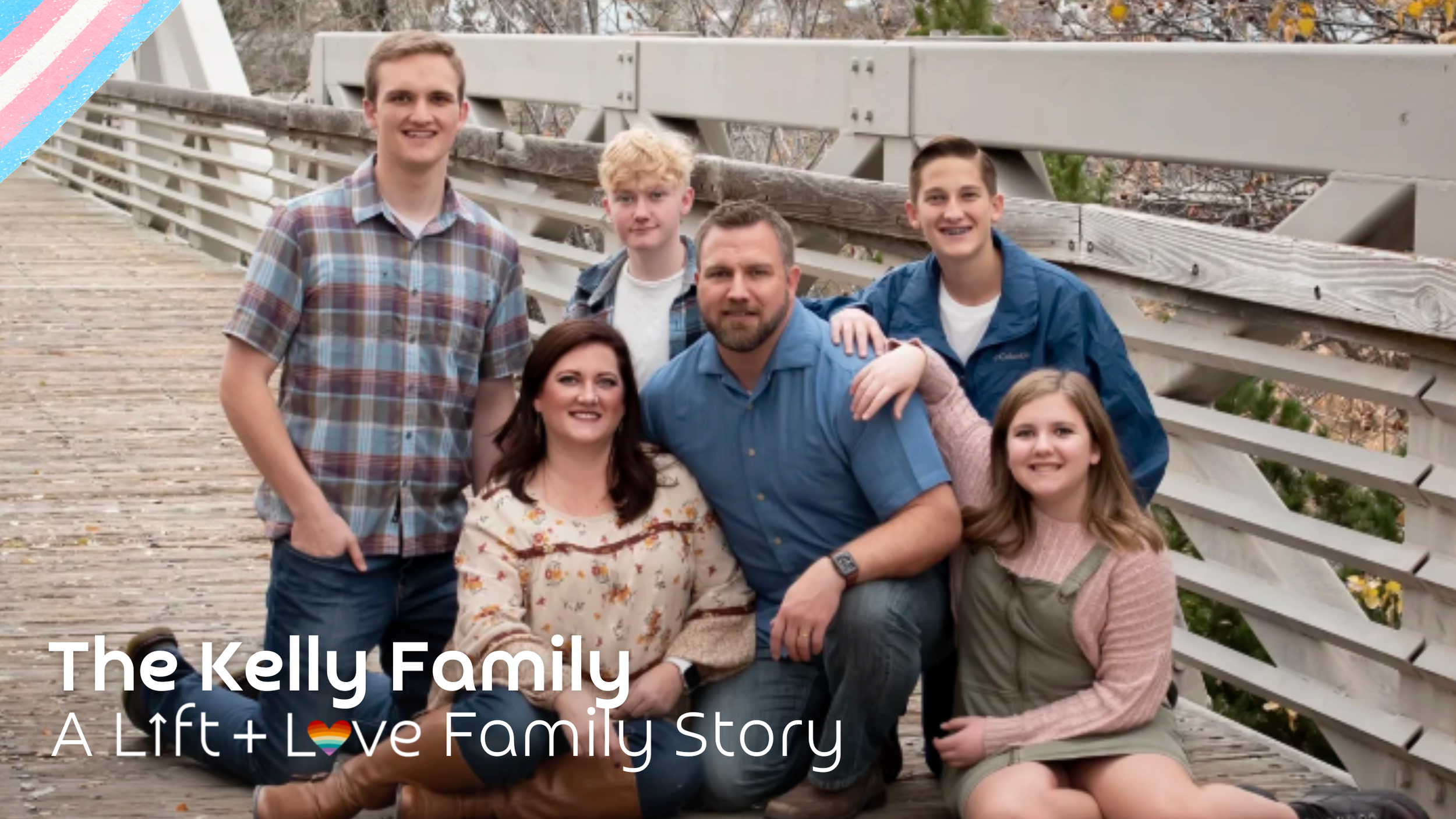 A family of seven posing on a wooden bridge outdoors, including four boys, two girls, and an adult man and woman, with trees and a cloudy sky in the background.