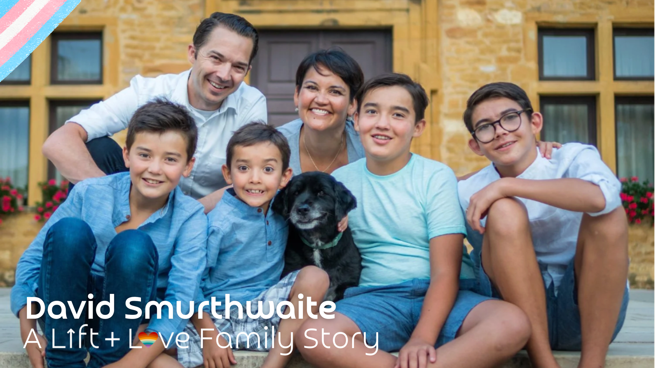 A happy family of six humans with a dog sitting on the steps of a yellow brick house with windows and flower boxes in the background.