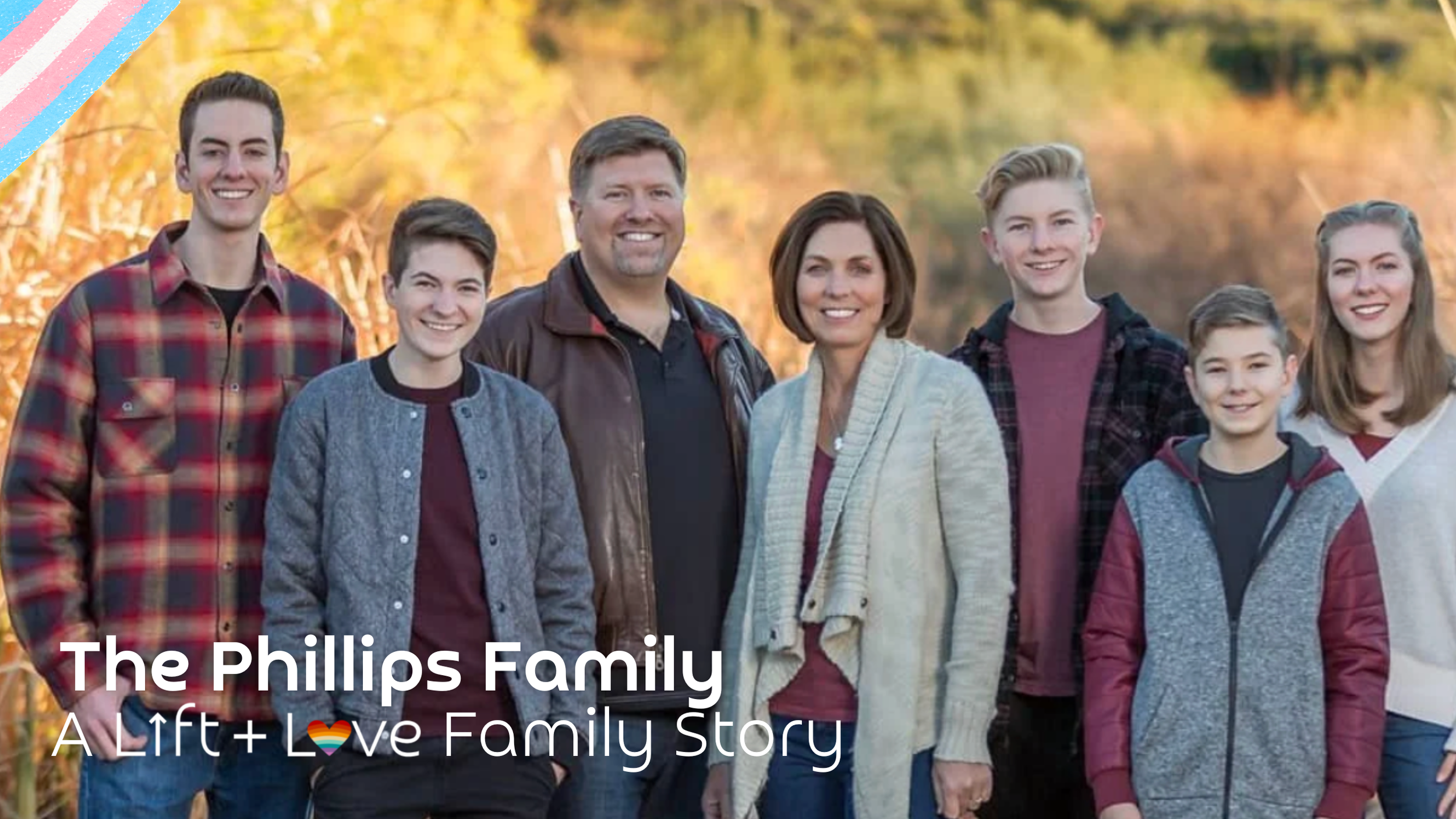 A family portrait outdoors during autumn, featuring seven members standing together and smiling, with fall foliage in the background.