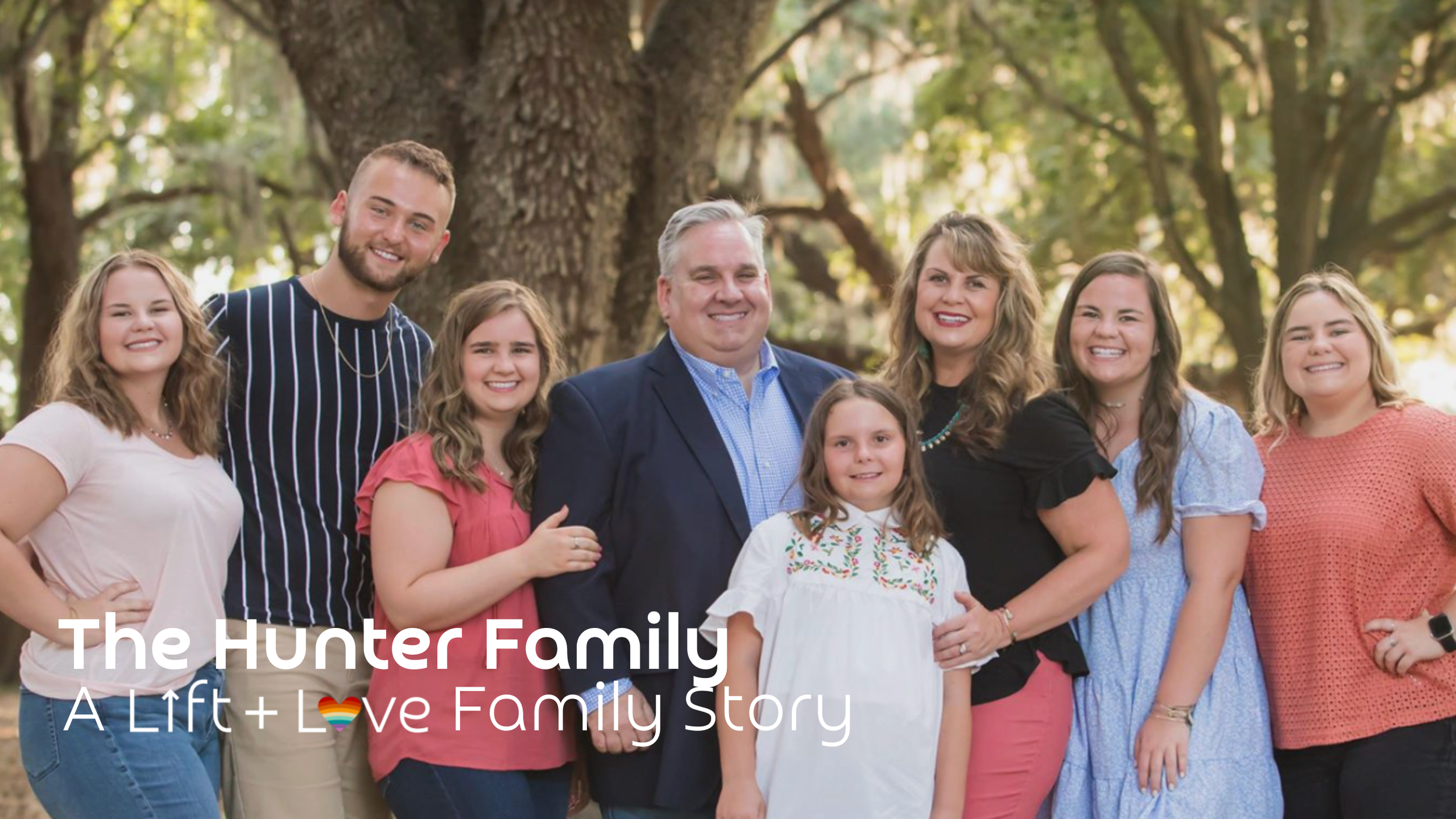Family of nine standing outdoors in front of a large tree, smiling at the camera. Text overlay reads "The Hunter Family: A Lift + Love Family Story."